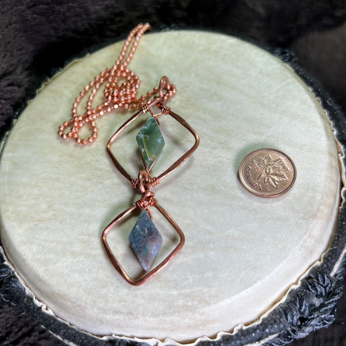 Hand made diamond motif copper necklace with moss agate gemstones on a white surface with a penny for scale.