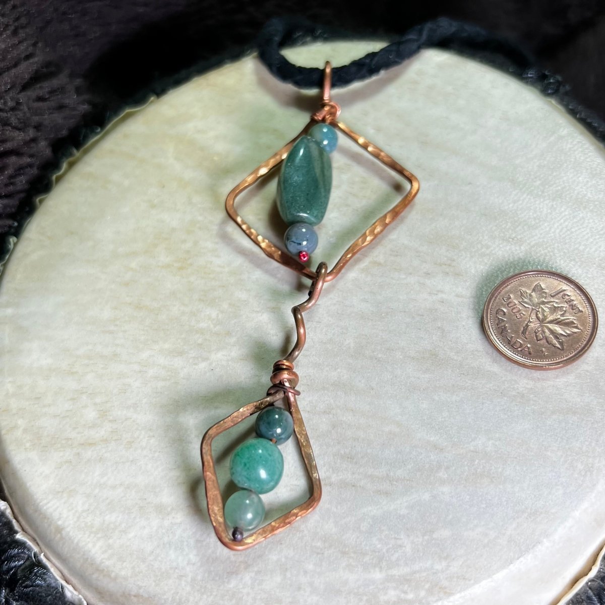 Diamond Motif necklace with moss agate stones and copper accents on a round beige surface.