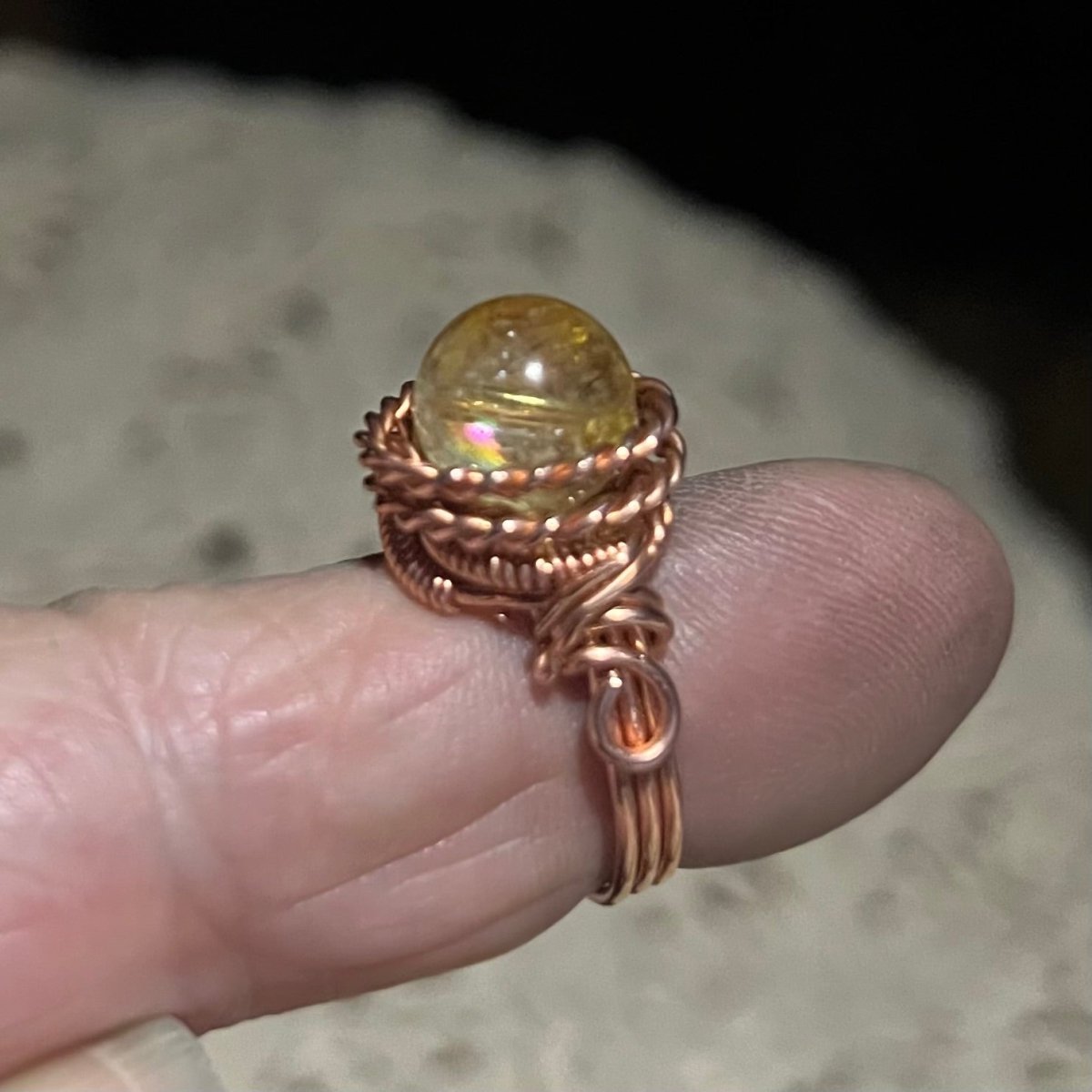 Copper wire-wrapped ring with a citrine gemstone on a finger against a blurred background