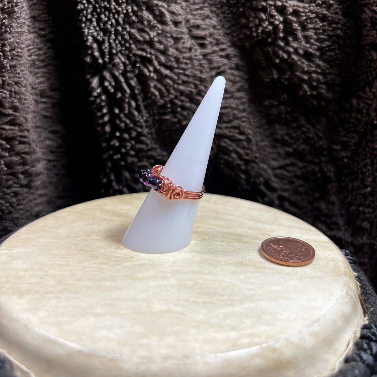 Ring on a white cone with a coin for scale against a textured brown background