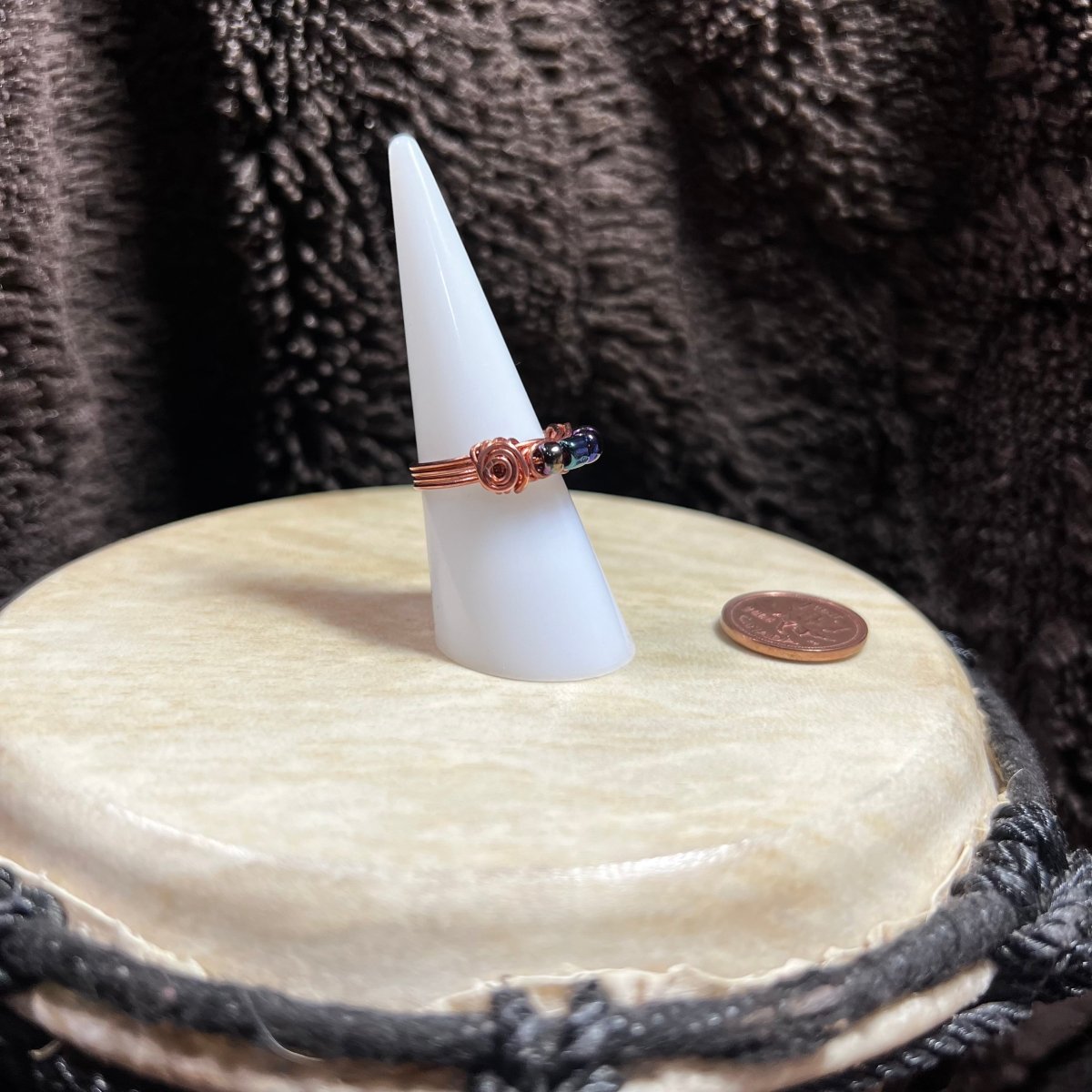 Ring on a cone-shaped stand with a coin for scale, against a textured brown background