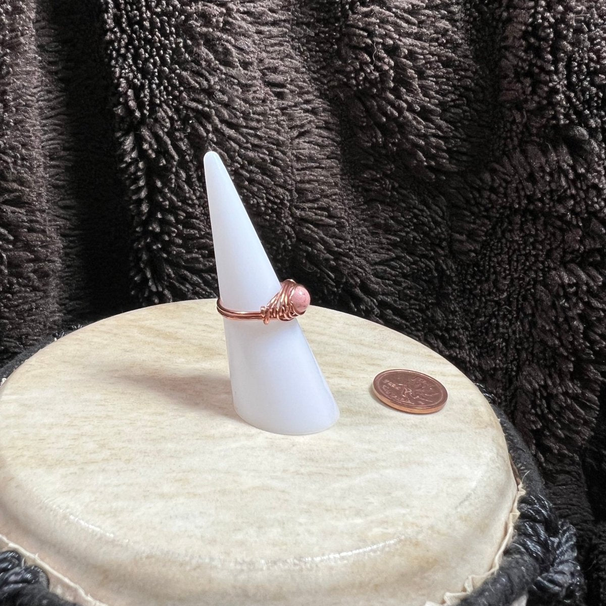 White cone-shaped object with a ring on top, placed on a round white surface with a dark textured background.
