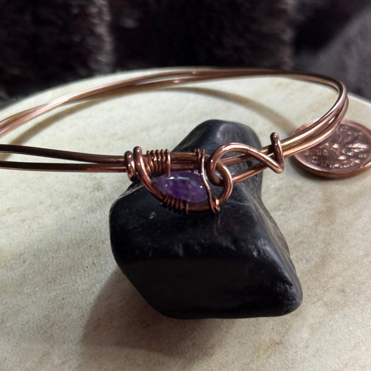 Close-up of the polished purple amethyst bead secured within the sculptural wire-wrapped joining point of a reclaimed copper bangle.