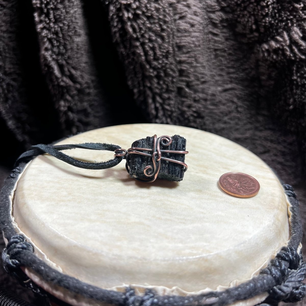 Black stone pendant on a leather cord with a coin on a white surface