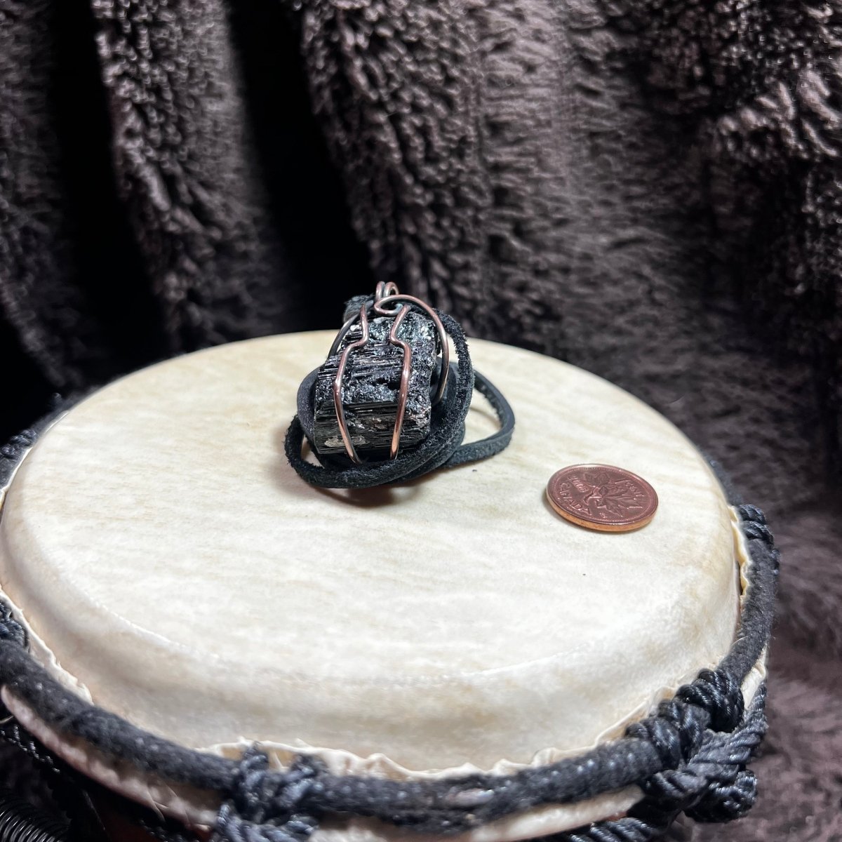Small black tourmaline crystal necklace on a white stone surface with a dark textured background