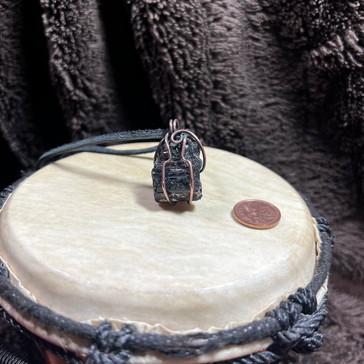 Black stone pendant on a leather cord with a coin on a white surface