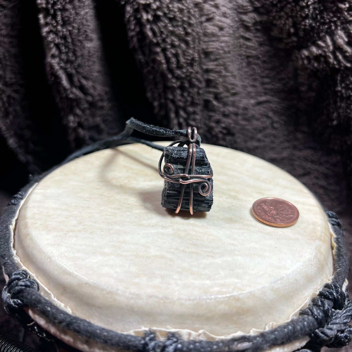 Black stone pendant on a leather cord with a coin on a white surface