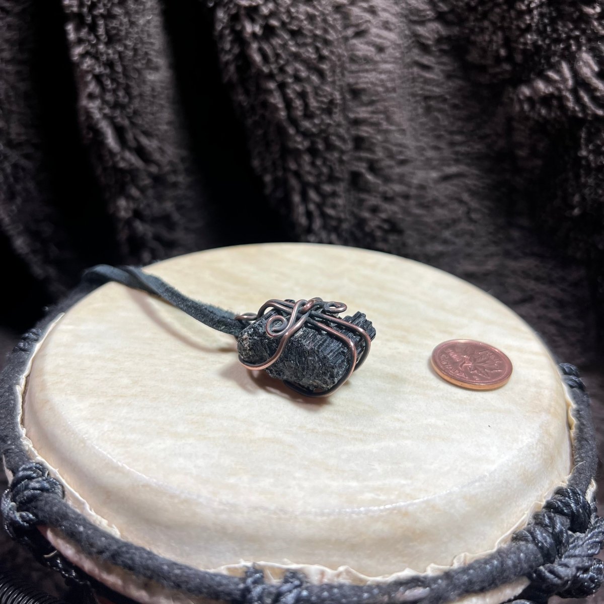 Black stone pendant on a leather cord with a coin on a white surface