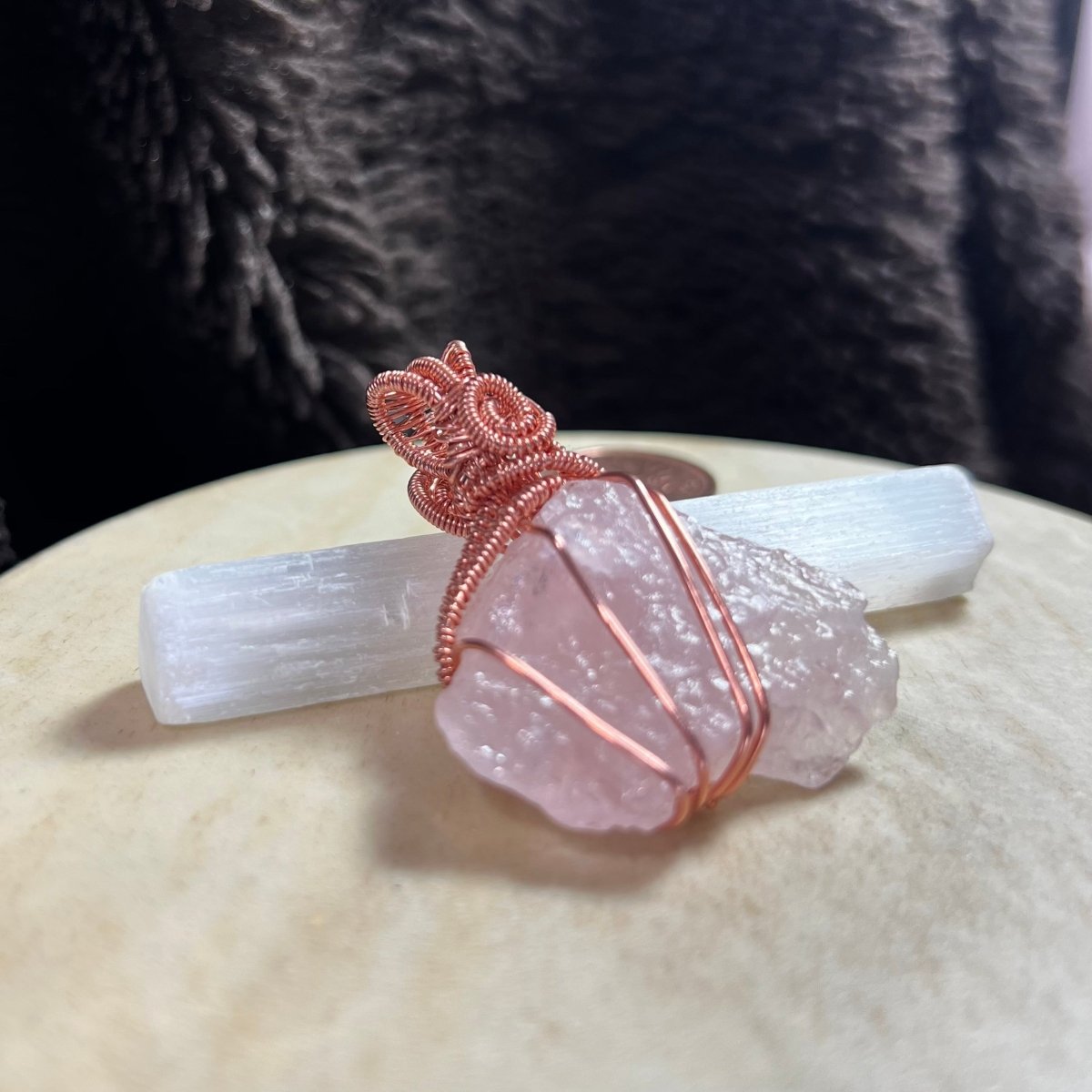 Rose quartz crystal with copper wire wrapping on a white stone