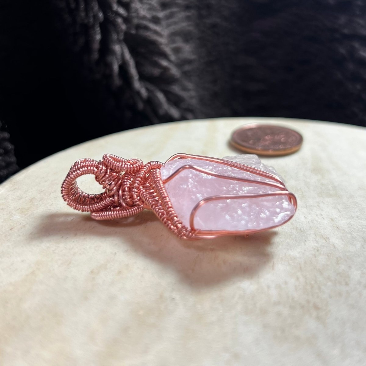 Rose quartz crystal with copper wire wrapping on a white stone