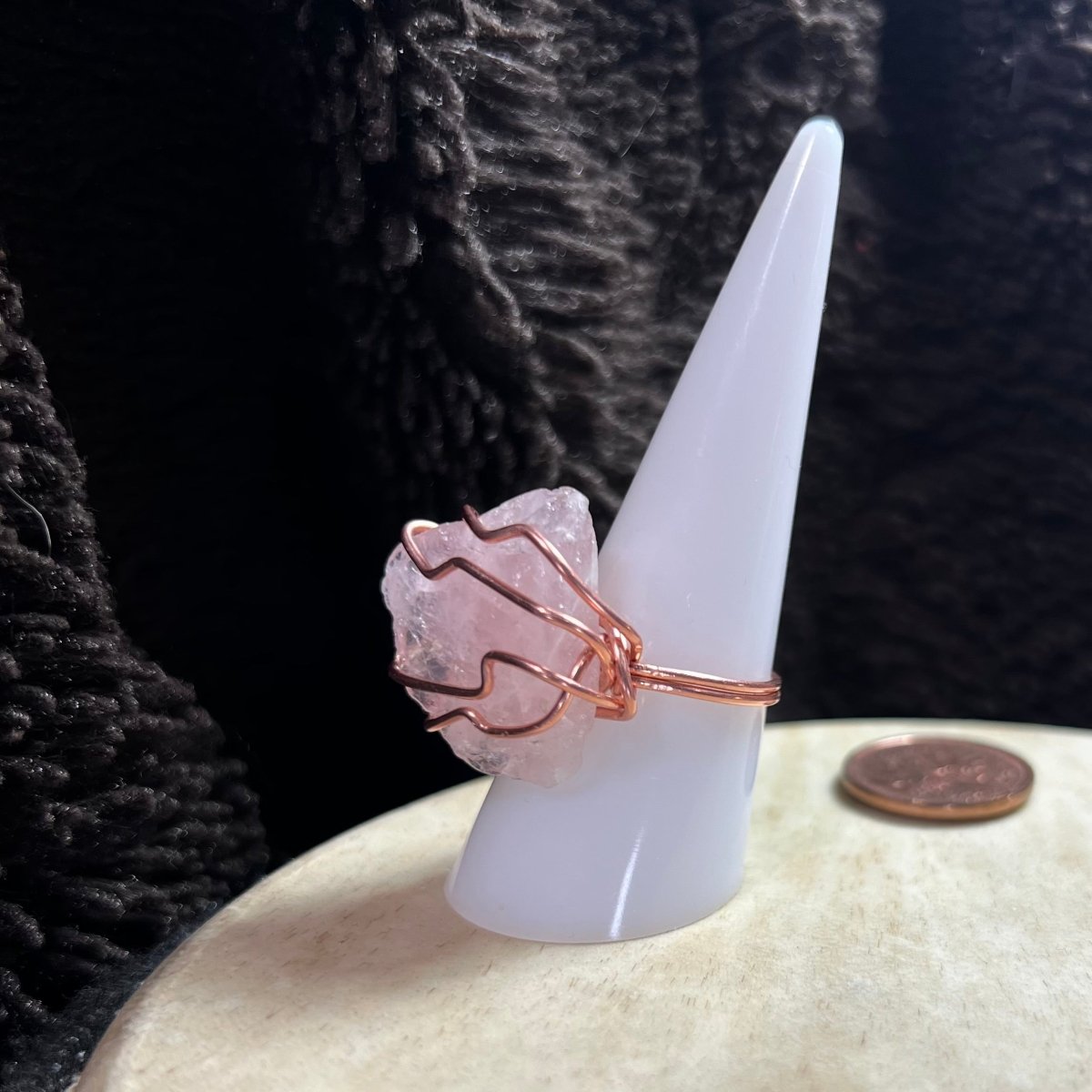 Crystal ring with rose quartz stone on a white cone-shaped object against a dark textured background