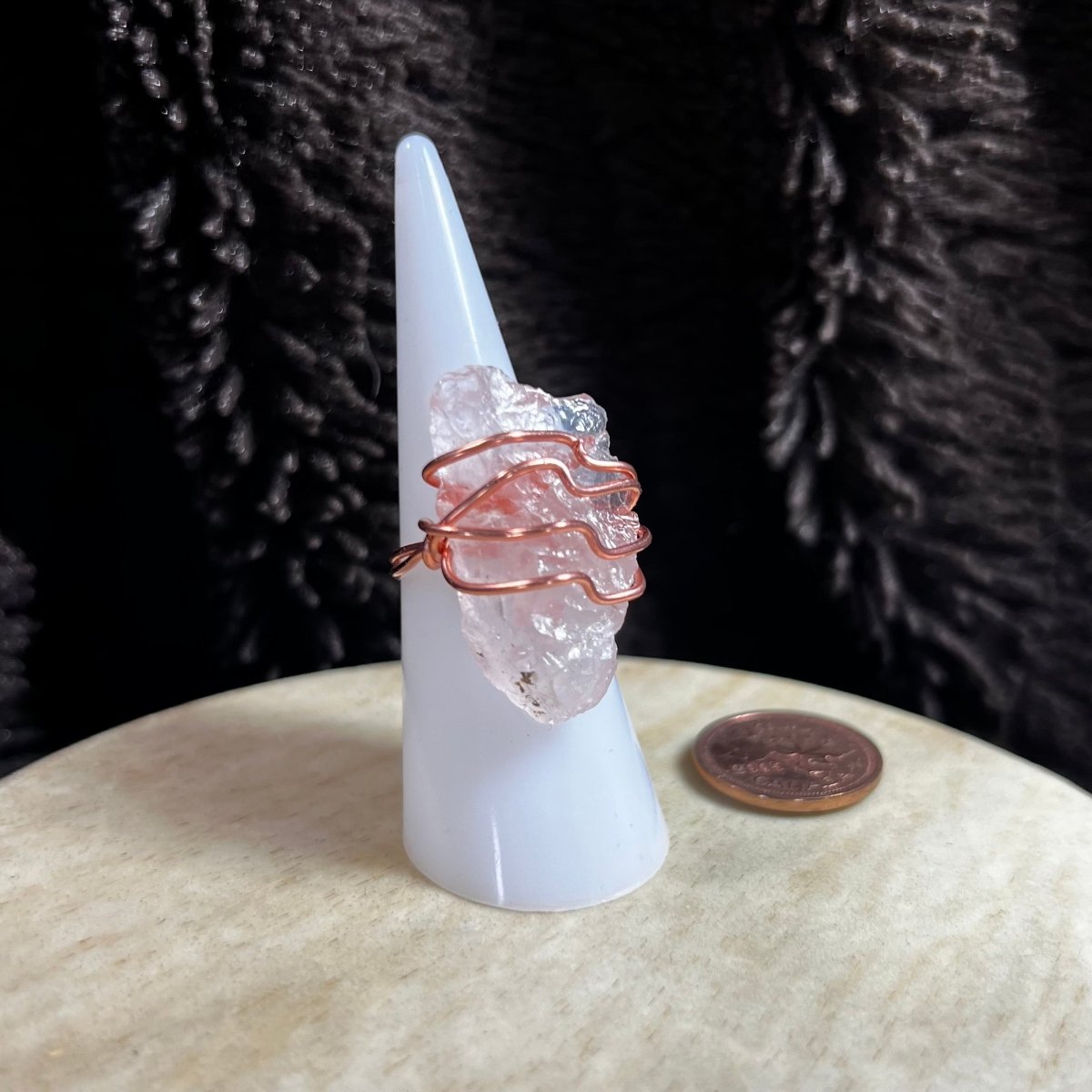 Rose quartz ring wire wrapped in copper on a white cone with a dark background