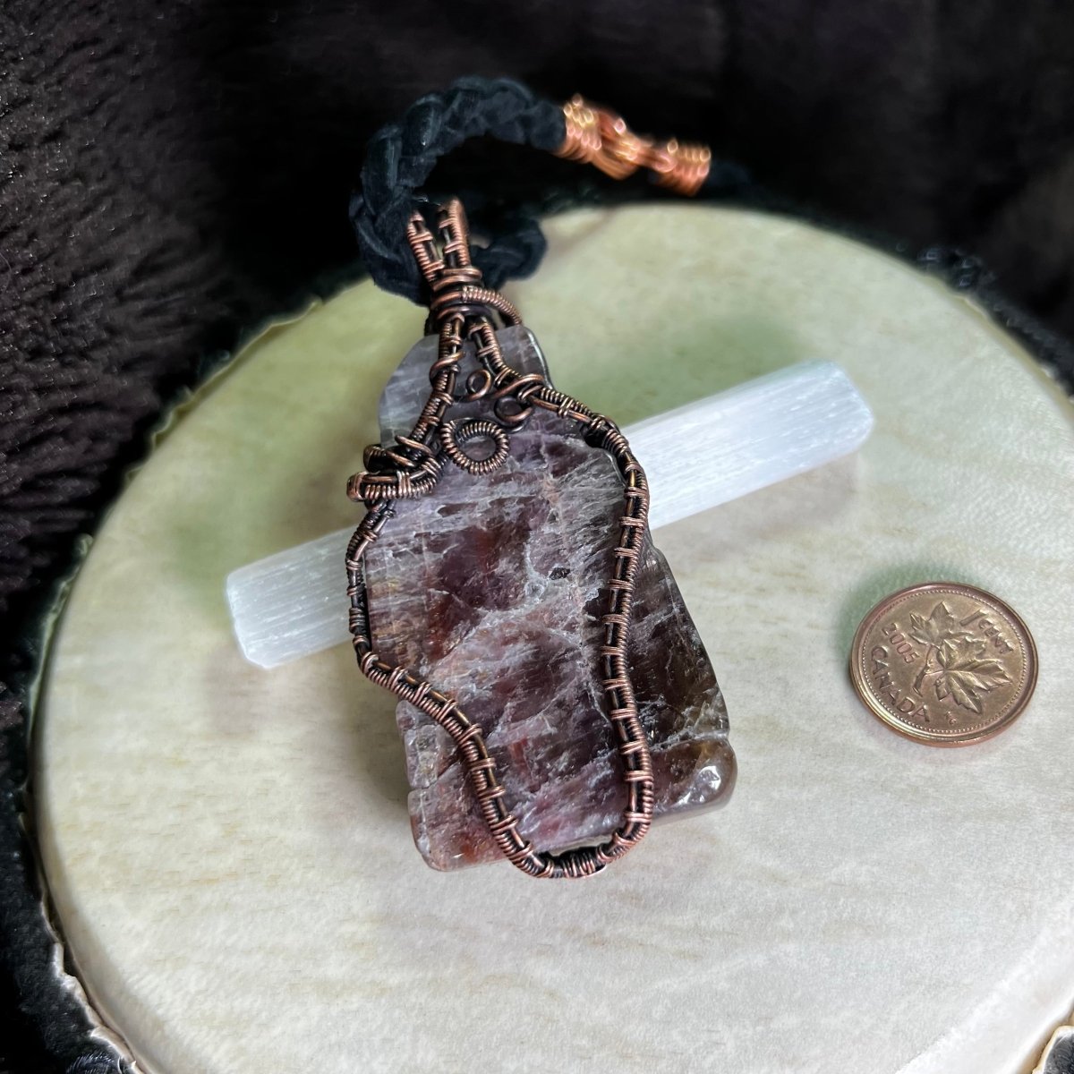 Super Seven crystal pendant with copper wire wrapping on a cream surface, next to a penny for scale.