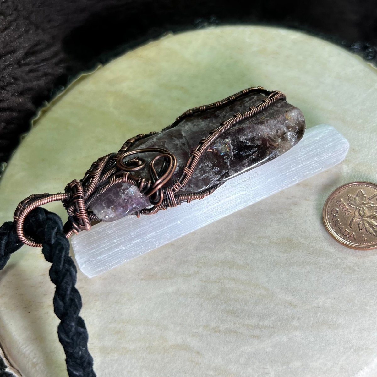 Necklace with super seven stone and copper wire on a selenite slab, next to a penny for scale.