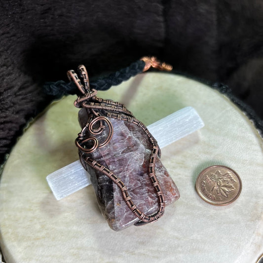 Copper-wrapped Super Seven stone pendant on a cream surface with a penny for scale.