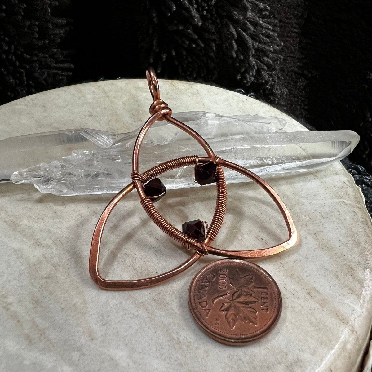 Copper wire-wrapped pendant with a coin on a marble surface with crystals in the background