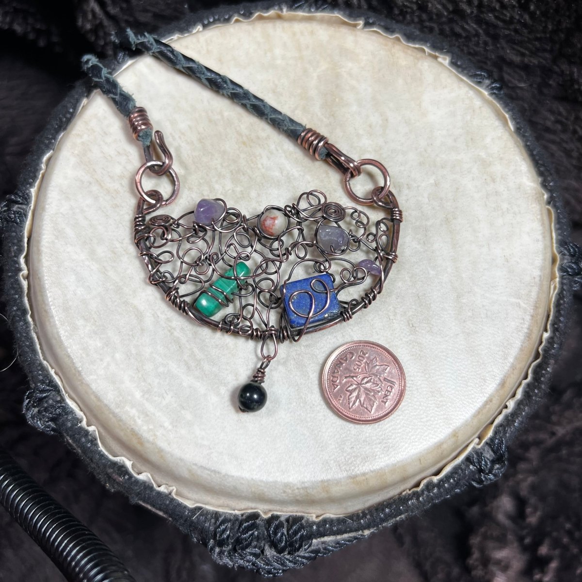 Handcrafted necklace with various stones and a blue pendant on a textured surface.