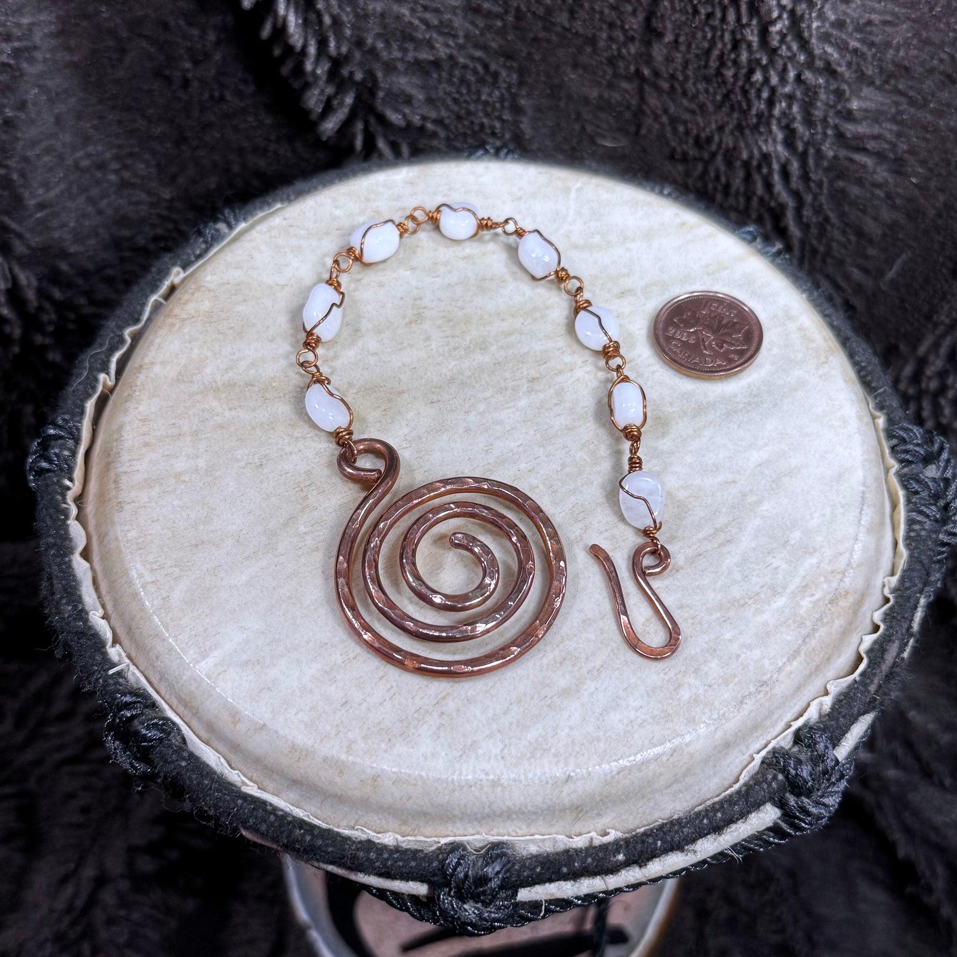 Open white moonstone bracelet with individually wire-wrapped stones, a large hammered spiral focal and handmade hook closure in reclaimed copper.
