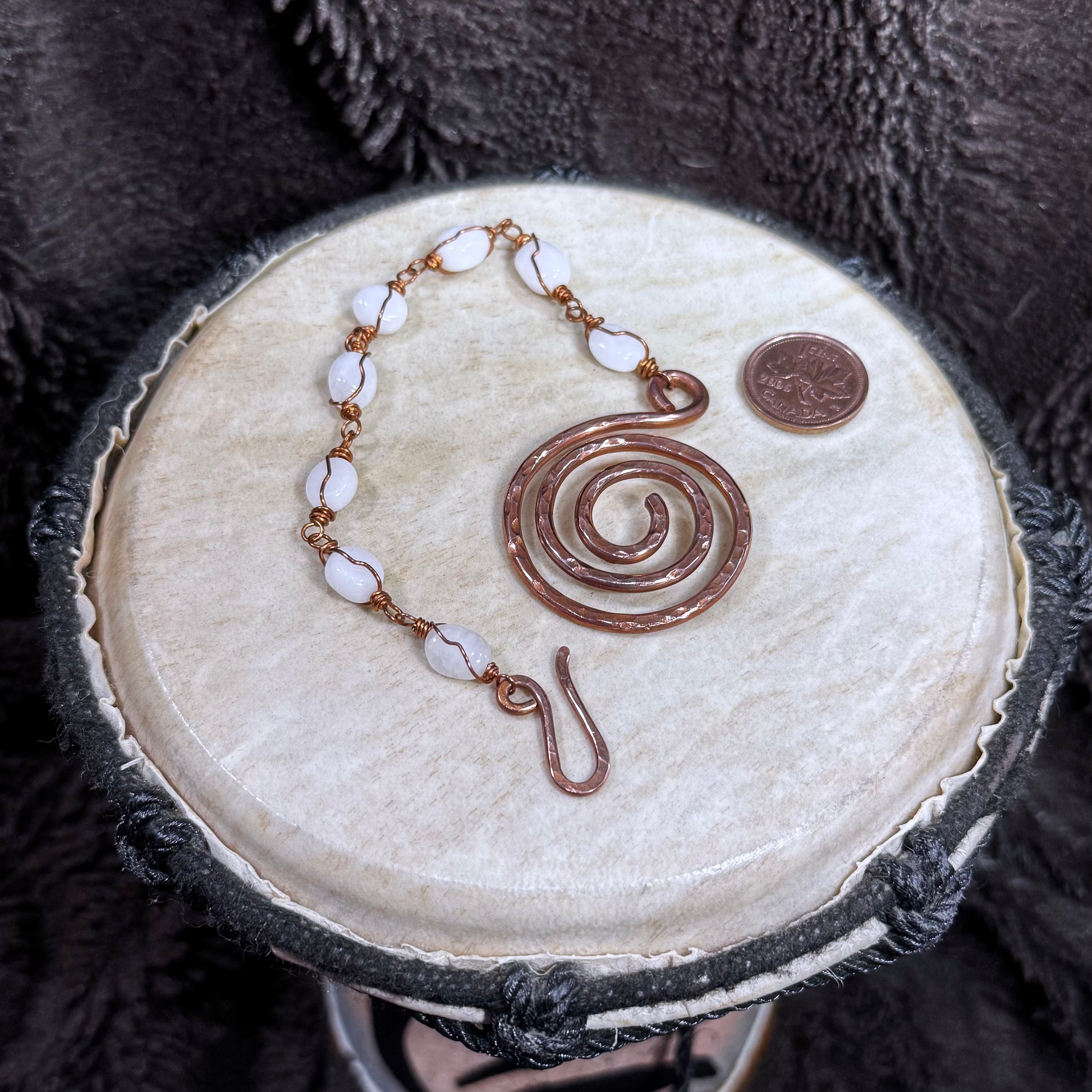 Detailed view of a handmade white moonstone bracelet with luminous stones, reclaimed copper links and a textured spiral focal.