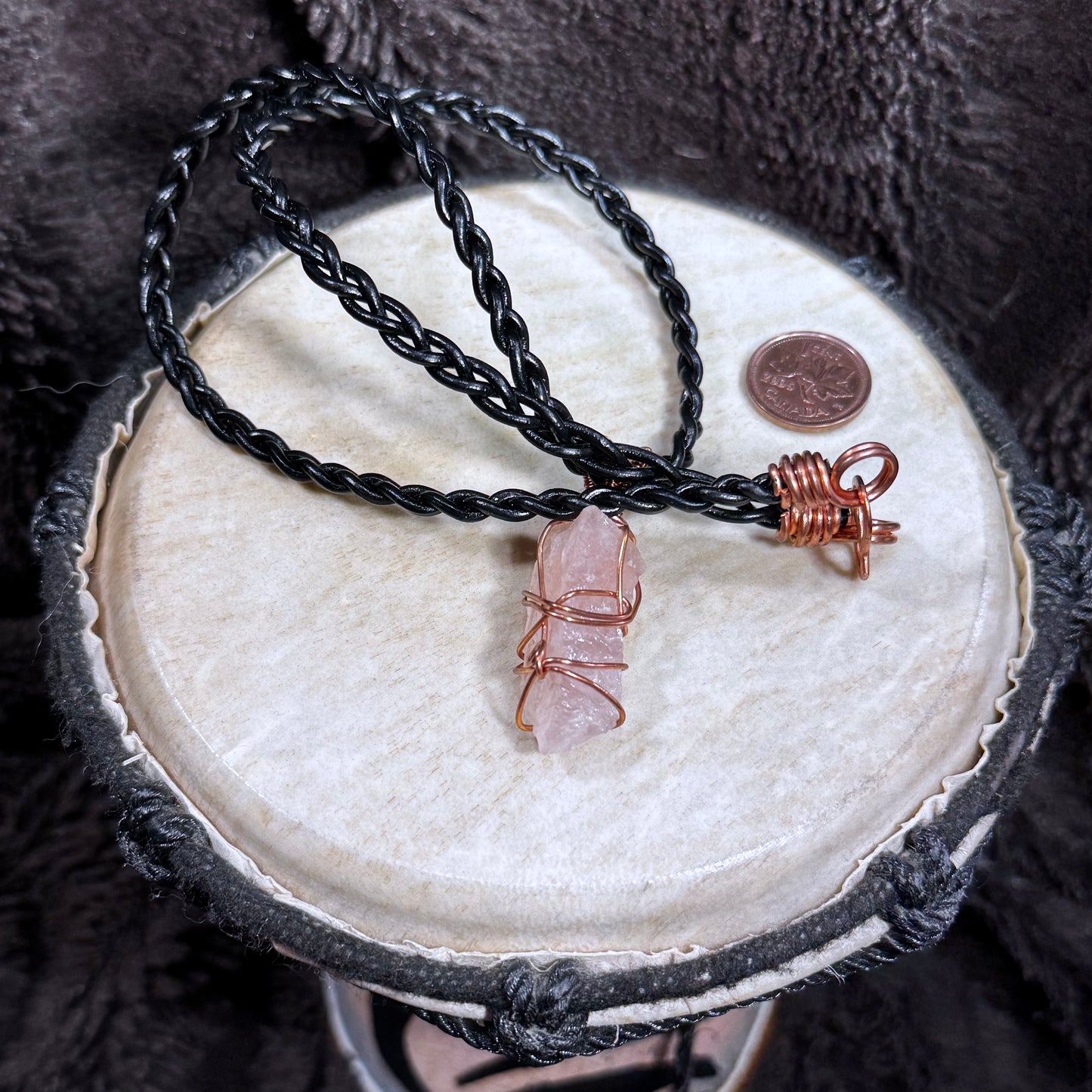 Back view of a raw Rose Quartz pendant secured with reclaimed copper wire on a black braided leather necklace.