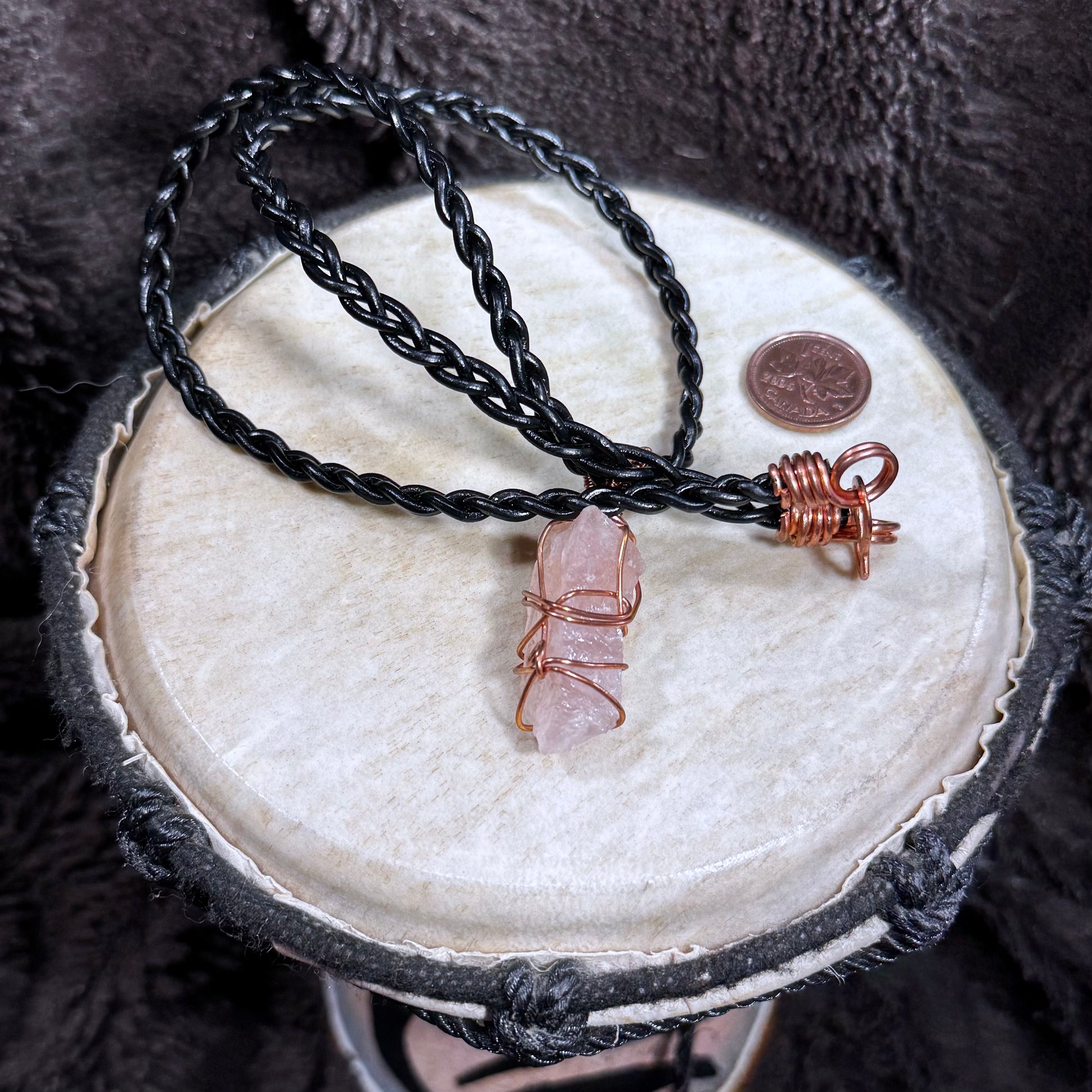 Back view of a raw Rose Quartz pendant secured with reclaimed copper wire on a black braided leather necklace.