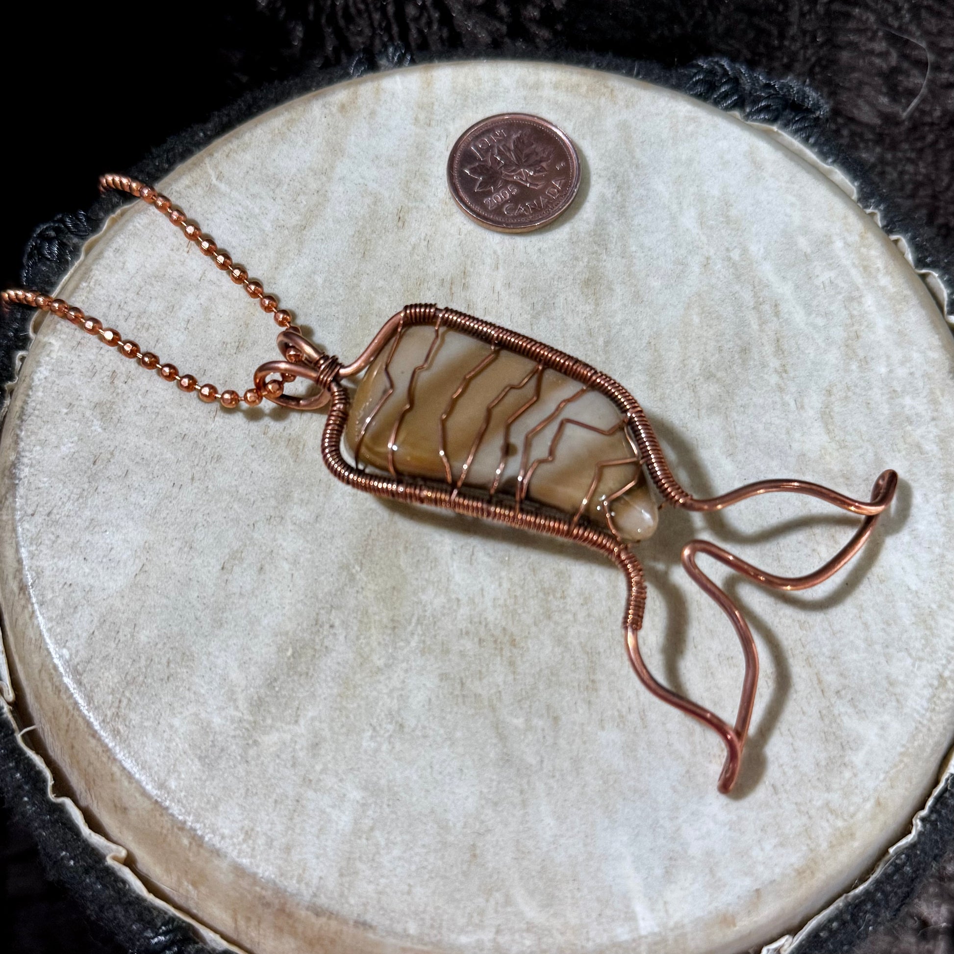Angled view of a handmade Bay of Fundy Jasper Mermaid Tail pendant showing the reclaimed copper wirework and naturally banded jasper from New Brunswick.