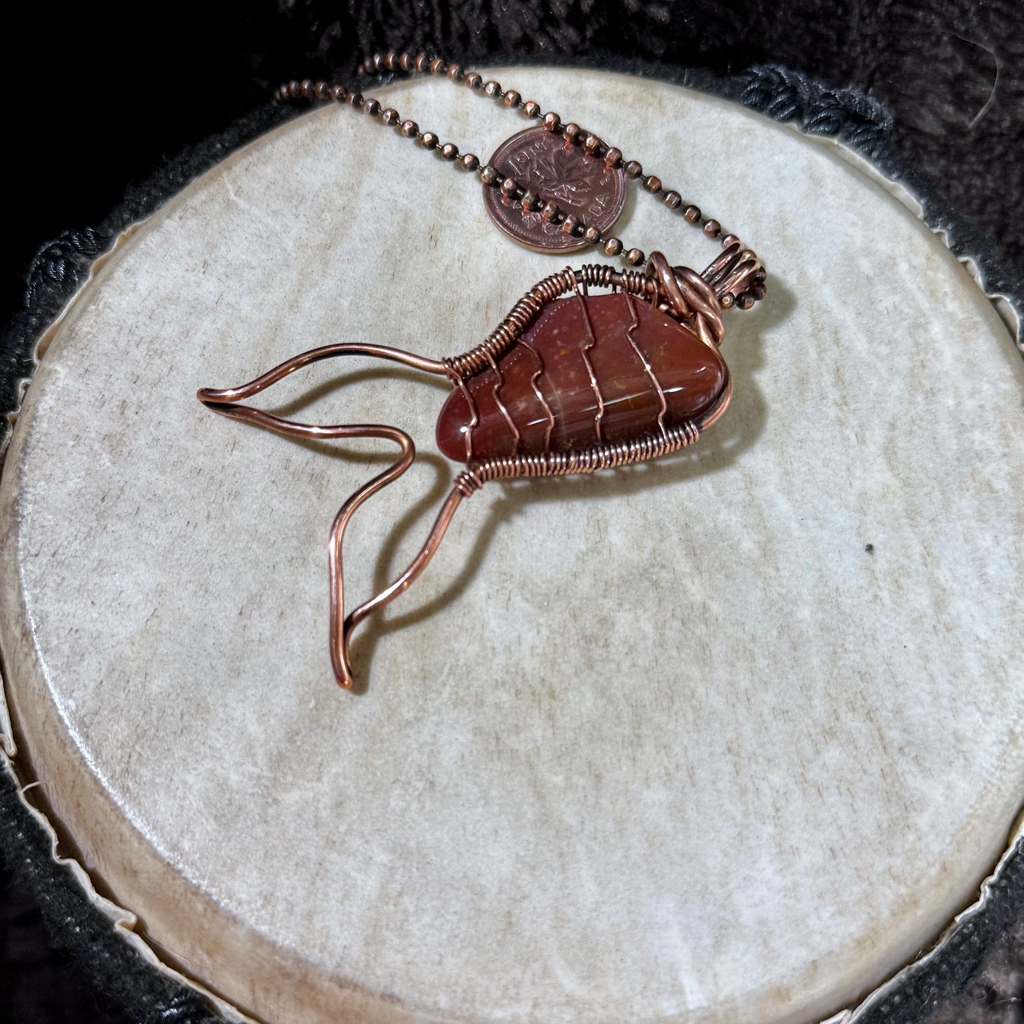 Side view of a handcrafted Red Jasper Mermaid Tail pendant showing the reclaimed copper wirework and the stone's natural red tones and banding.