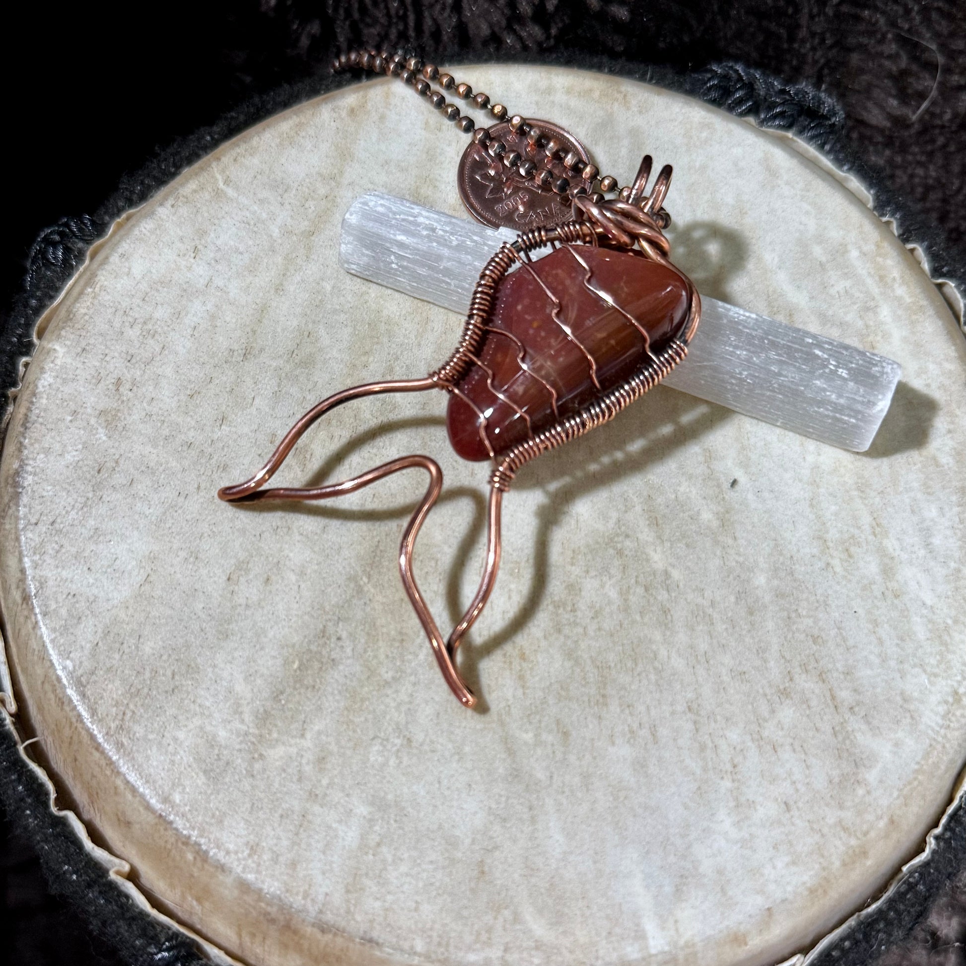 Red Jasper Mermaid Tail pendant displayed on a selenite wand, highlighting the polished reclaimed copper wire wrapping and one-of-a-kind natural gemstone.