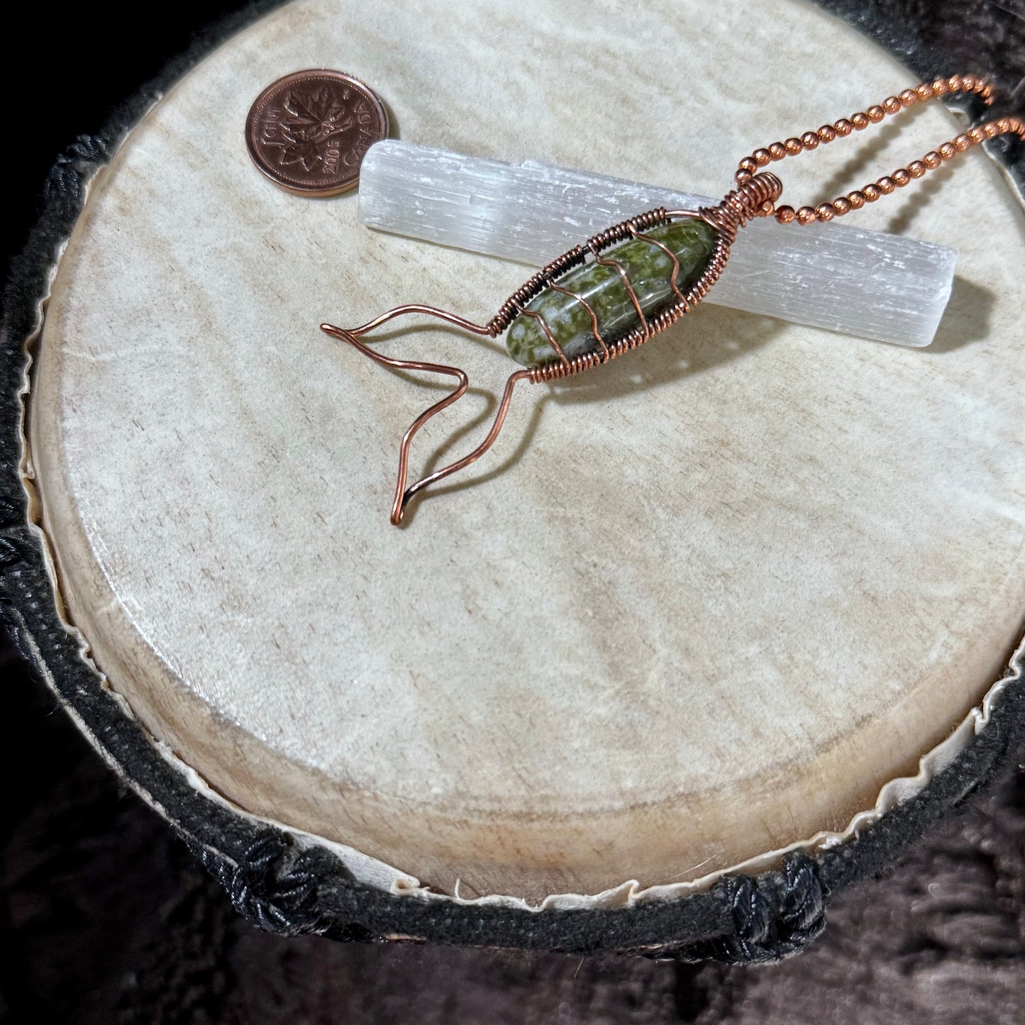 Bay of Fundy Green Epidote Mermaid Tail Necklace displayed with a Canadian penny for scale, showcasing reclaimed copper wirework and a naturally patterned green gemstone.