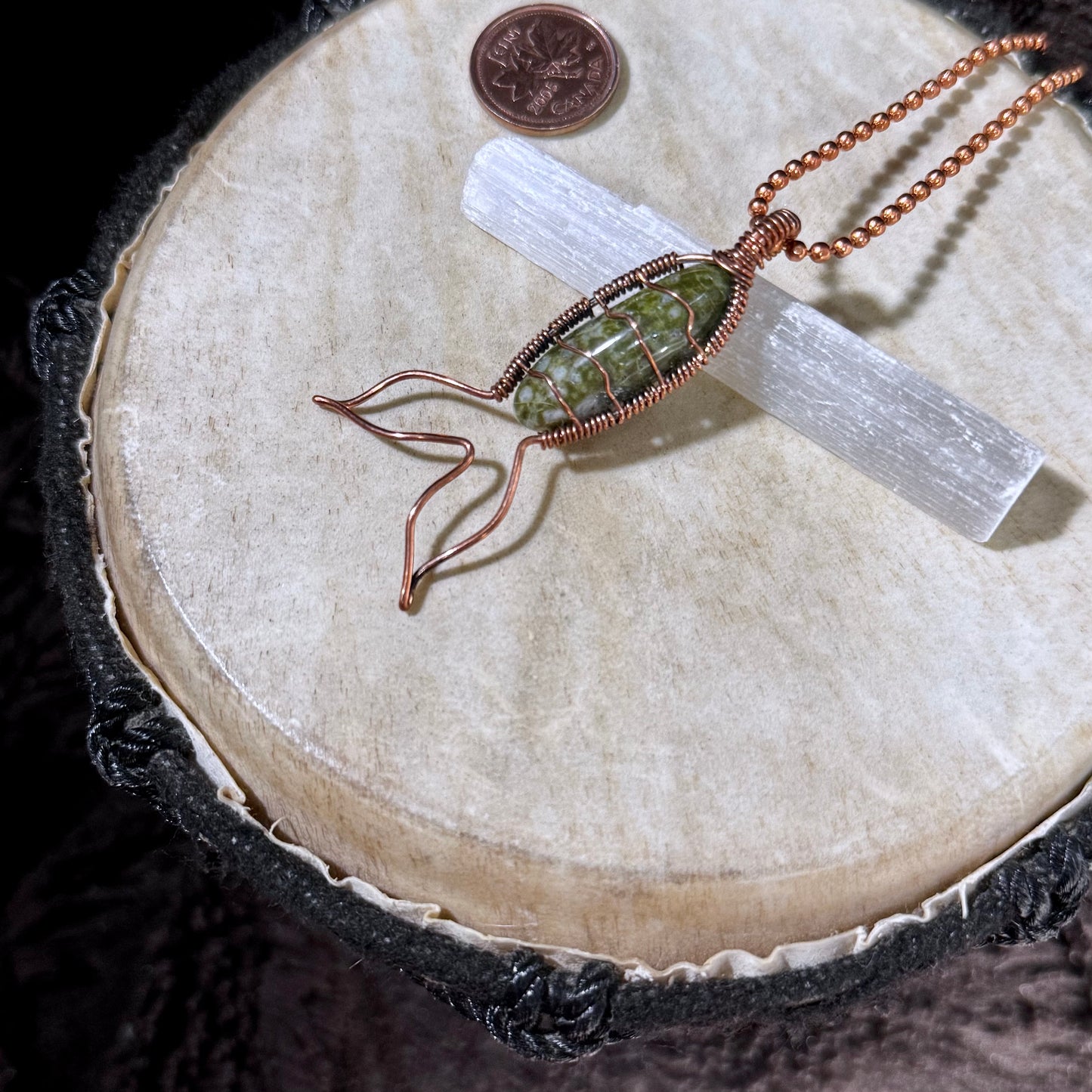Handcrafted Bay of Fundy Green Epidote Mermaid Tail Necklace resting on a selenite wand, highlighting the natural green stone, reclaimed copper wrapping, and flowing mermaid tail design.
