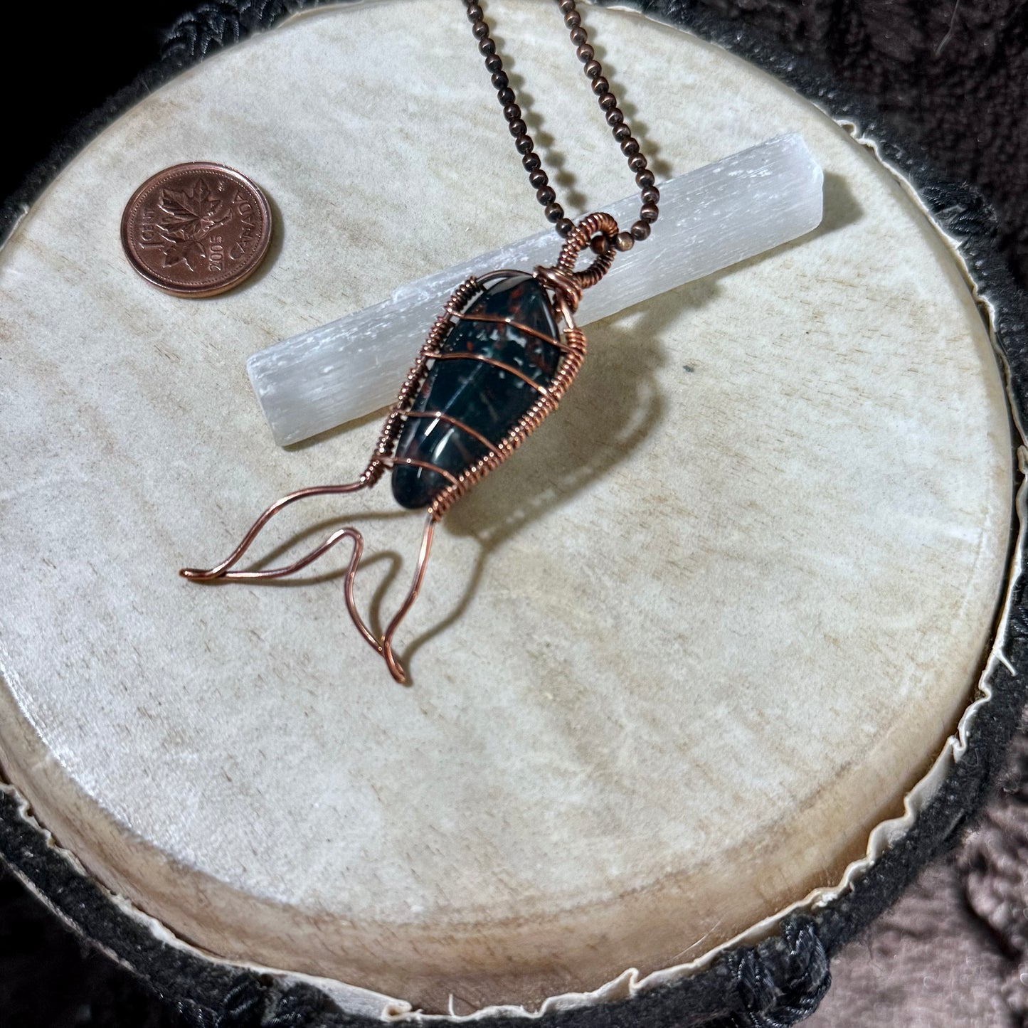 Bay of Fundy Bloodstone Mermaid Tail Necklace resting on a selenite wand, highlighting the natural gemstone, reclaimed copper craftsmanship, and elegant mermaid tail silhouette.