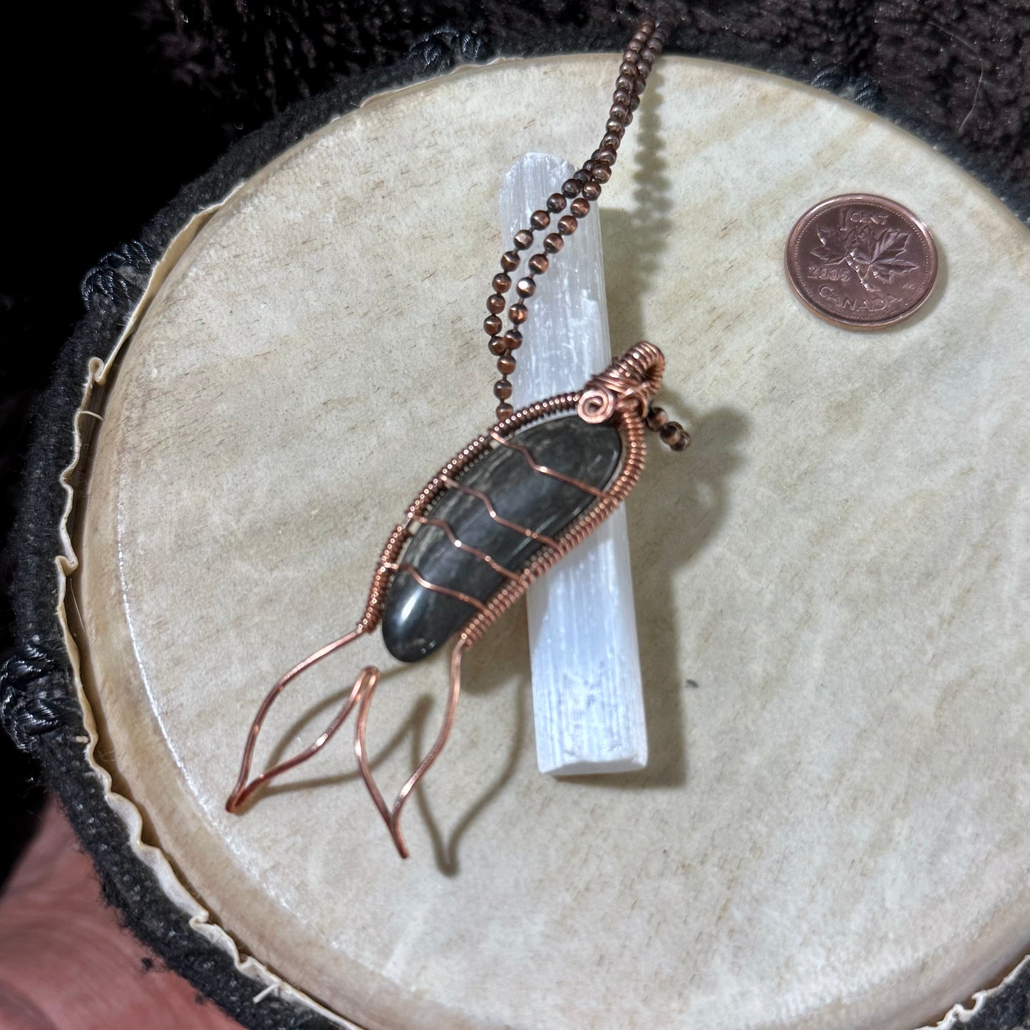 Black agate Mermaid Tail necklace displayed on a selenite wand, showcasing the dark banding of the Bay of Fundy stone and handcrafted reclaimed copper details.