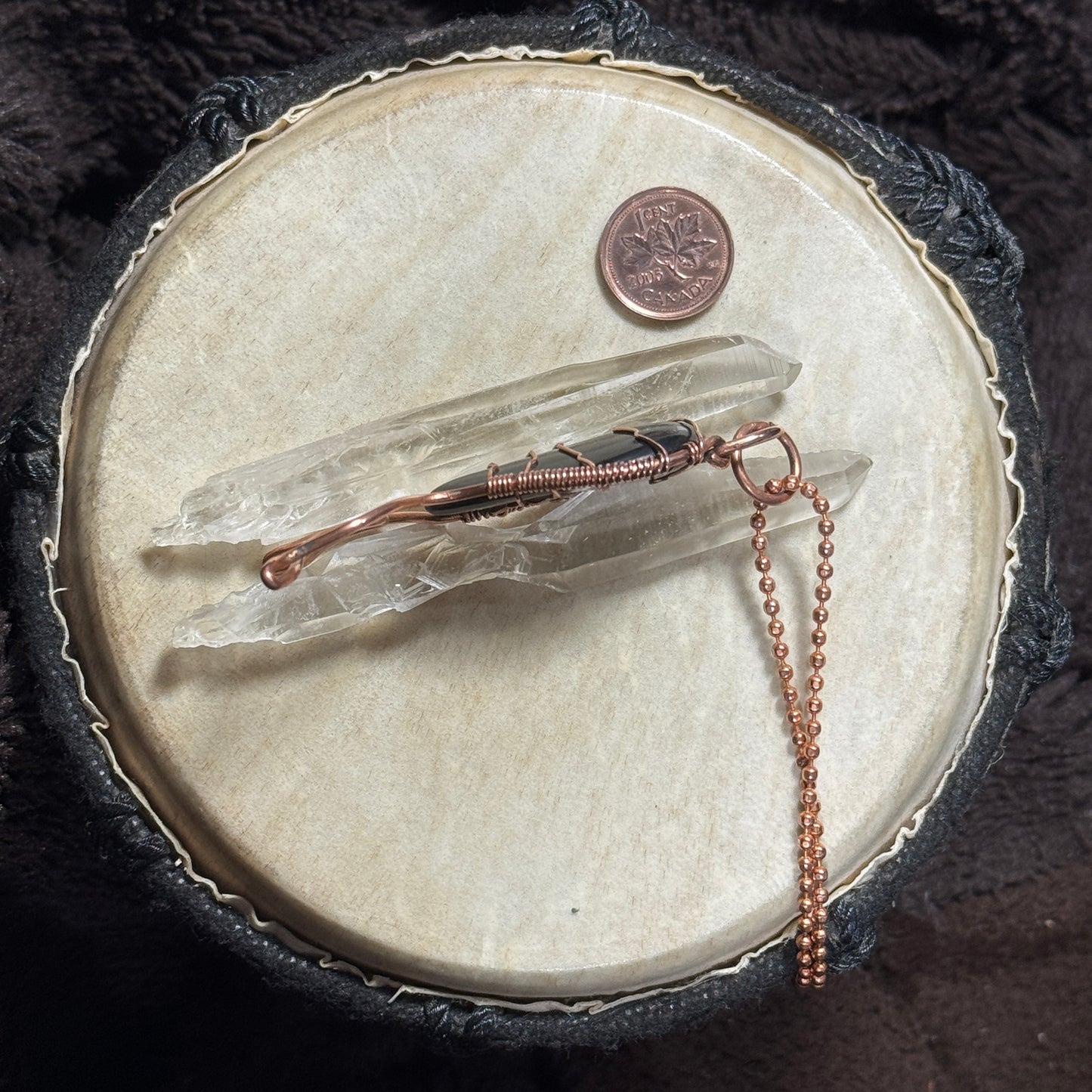 Side profile of a handmade black agate Mermaid Tail pendant in raw copper displayed with clear crystal points.