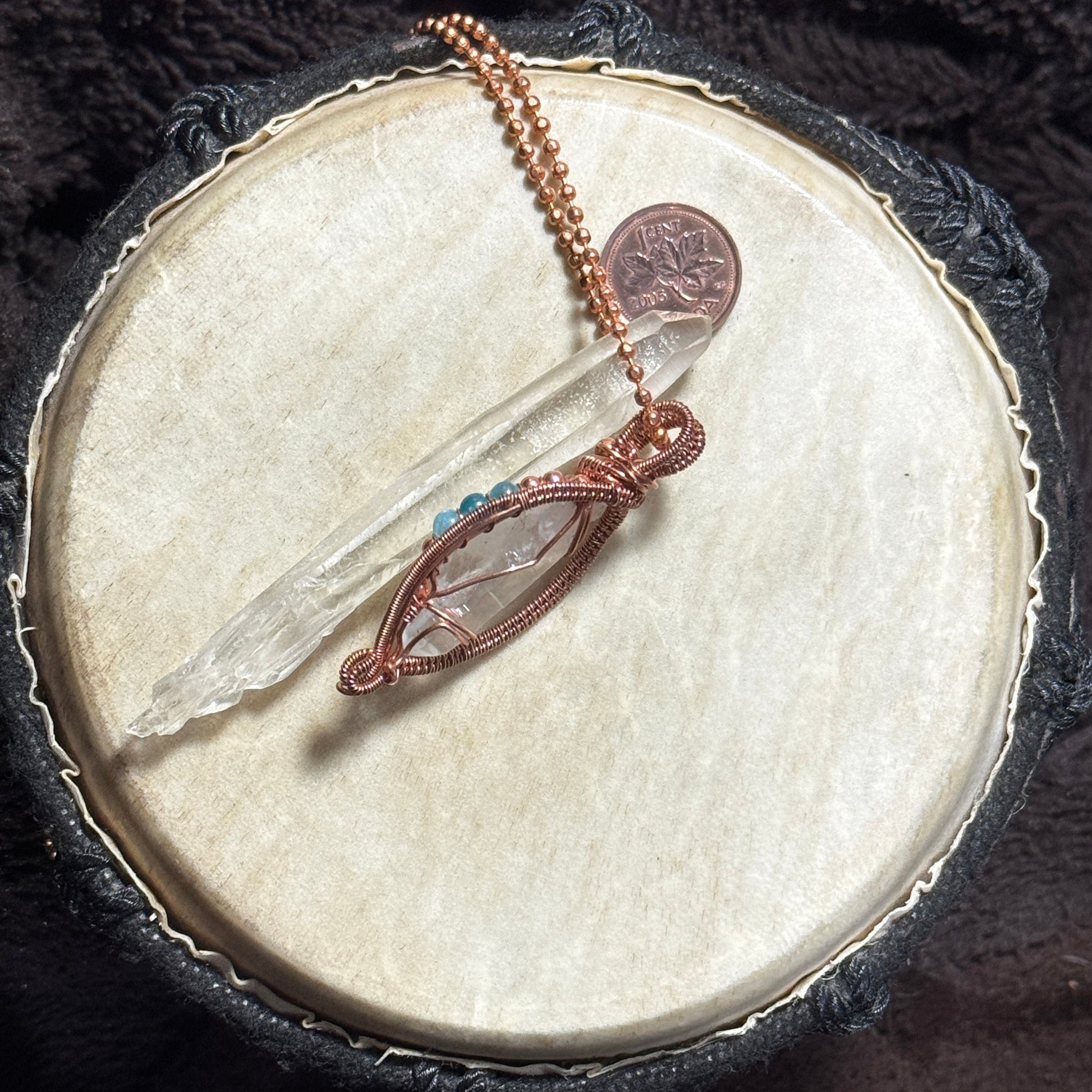 Side view of a raw copper woven Lemurian crystal pendant with blue apatite and copper bead accents, displayed with a clear crystal point.