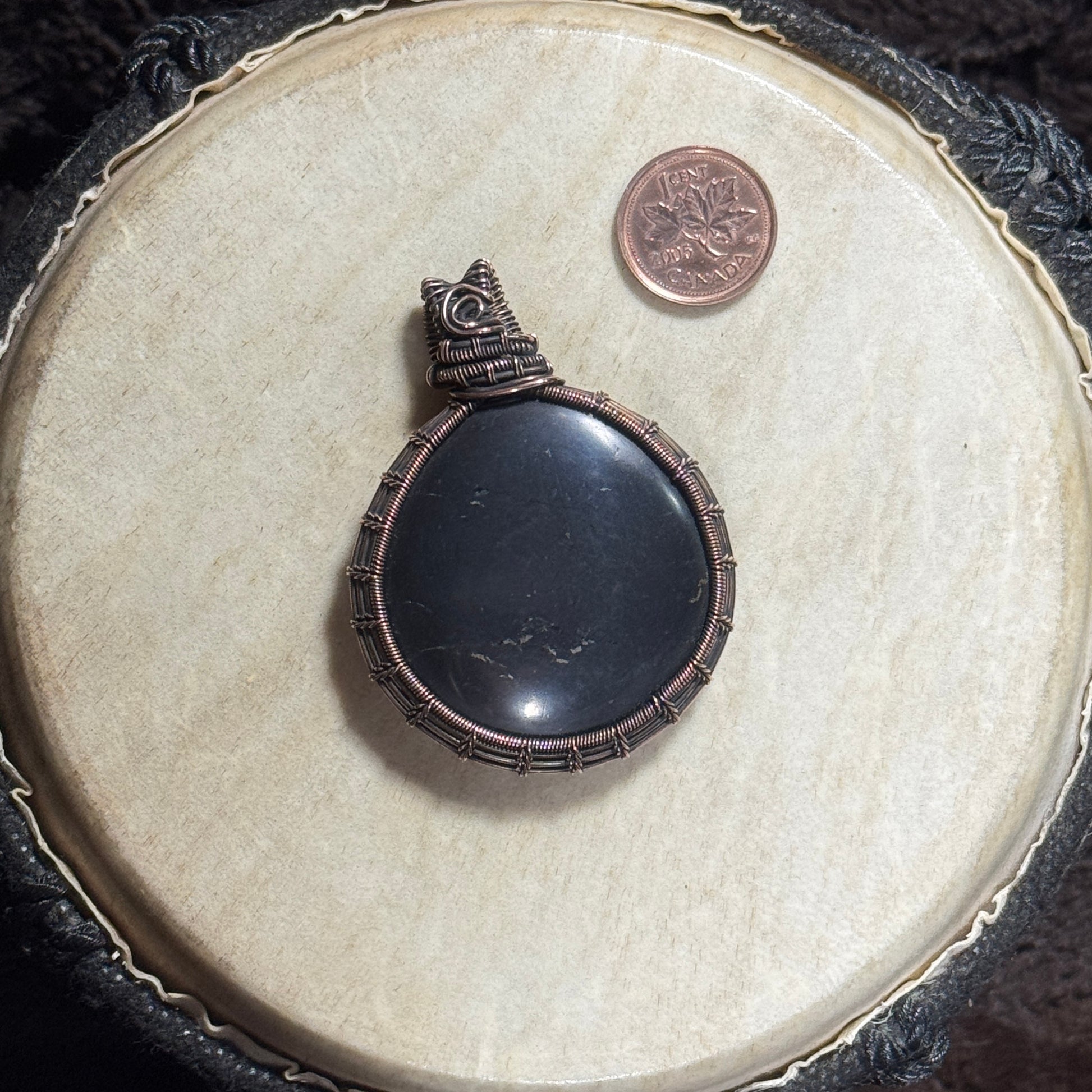 Front view of a handmade shungite pendant with tiny pyrite flecks wrapped in intricate fine copper wire and finished with a dark patina.