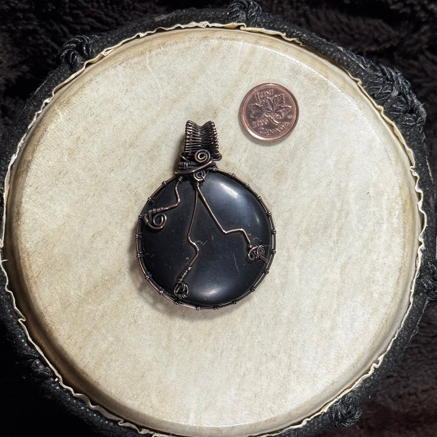 Reverse view of a round shungite pendant showing decorative copper wirework and a detailed patinated fine-wire frame.
