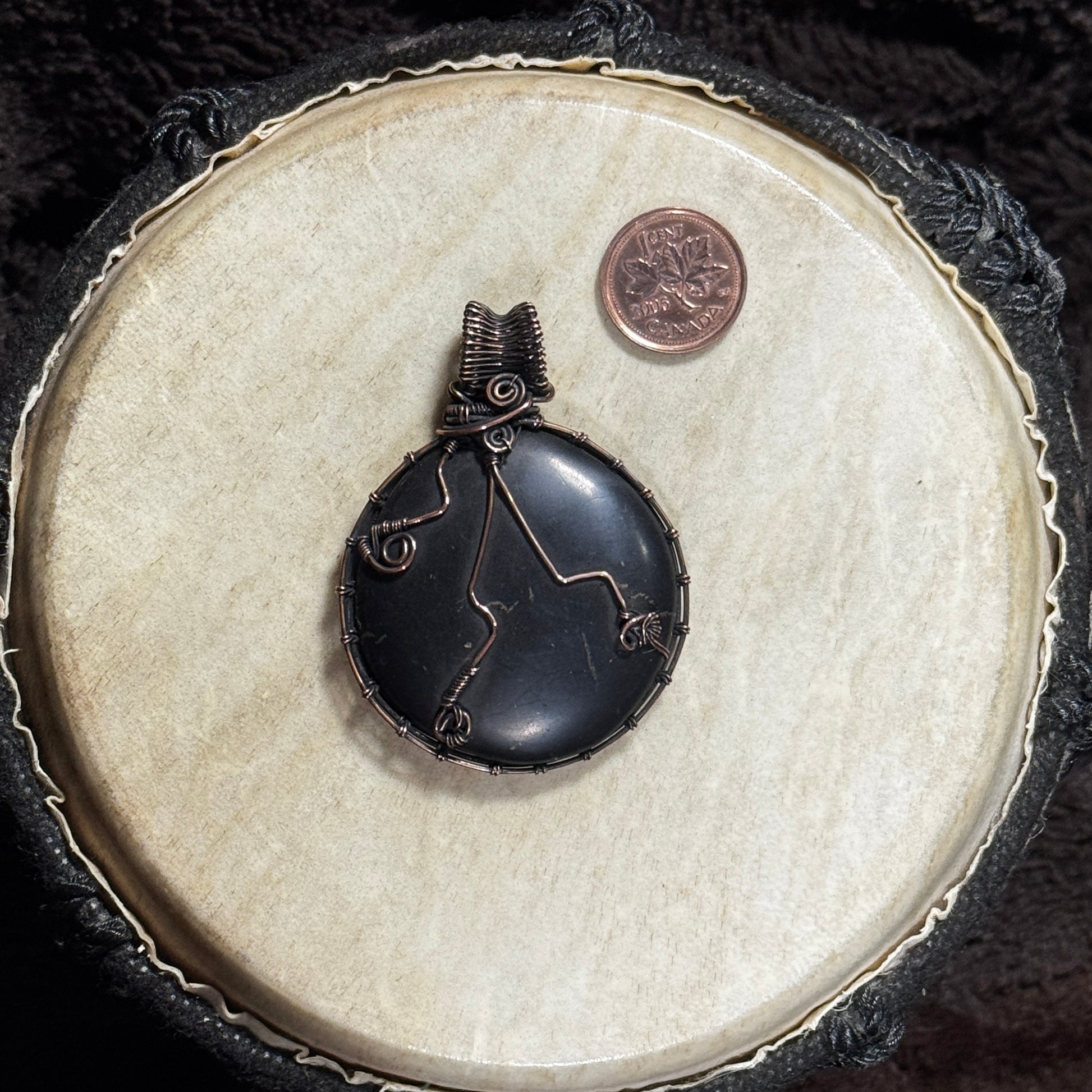 Reverse view of a round shungite pendant showing decorative copper wirework and a detailed patinated fine-wire frame.
