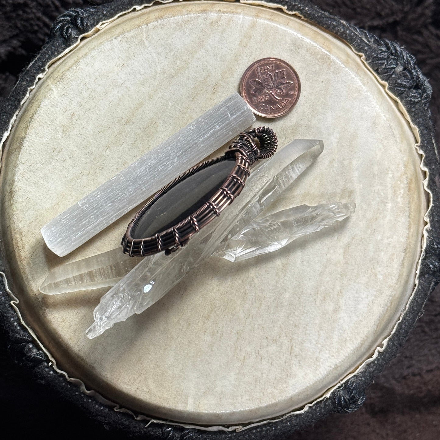 Side profile of a handcrafted shungite pendant displayed with crystal points, showing the depth of the stone and fine woven copper setting.
