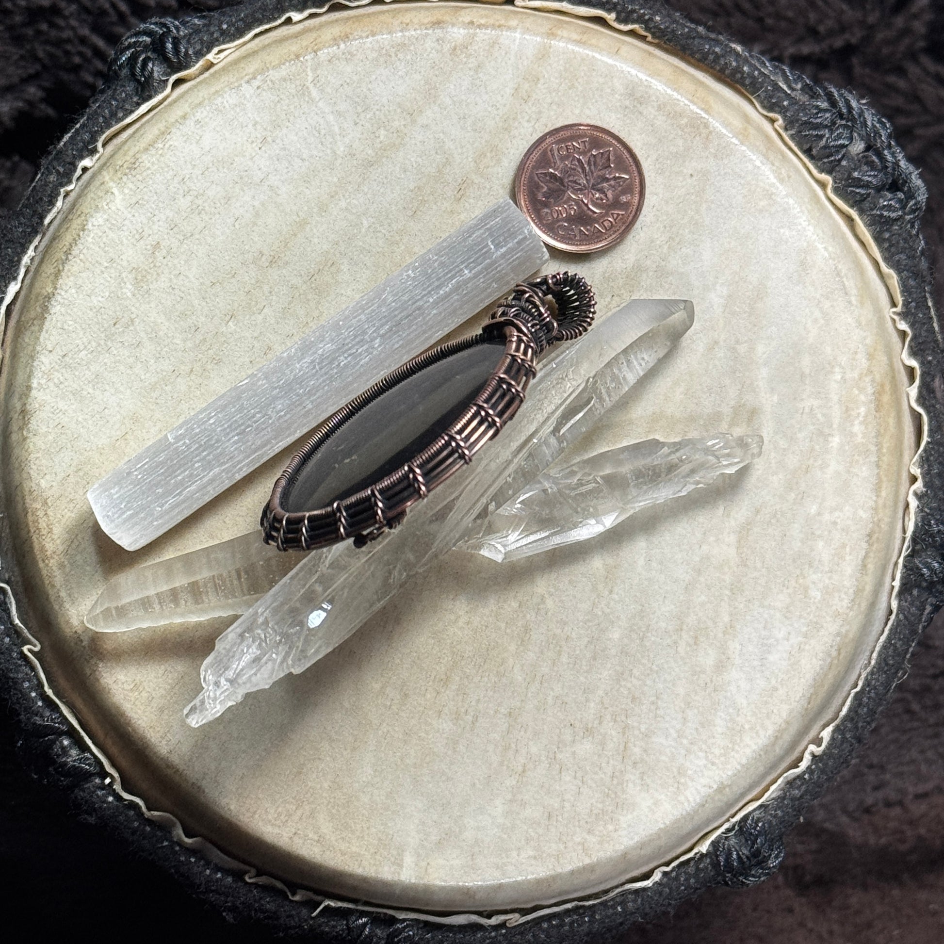 Side profile of a handcrafted shungite pendant displayed with crystal points, showing the depth of the stone and fine woven copper setting.
