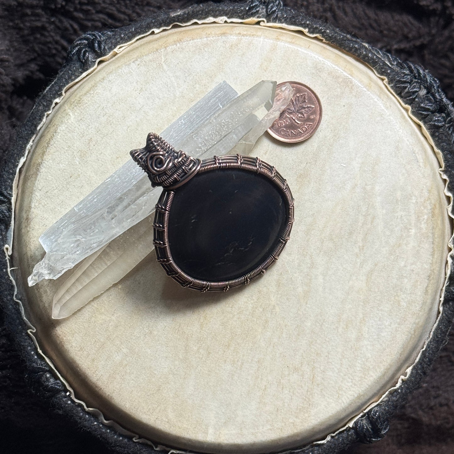 Front display view of a dark shungite pendant wrapped in patinated copper with intricate fine-wire weaving and subtle natural pyrite flecks.