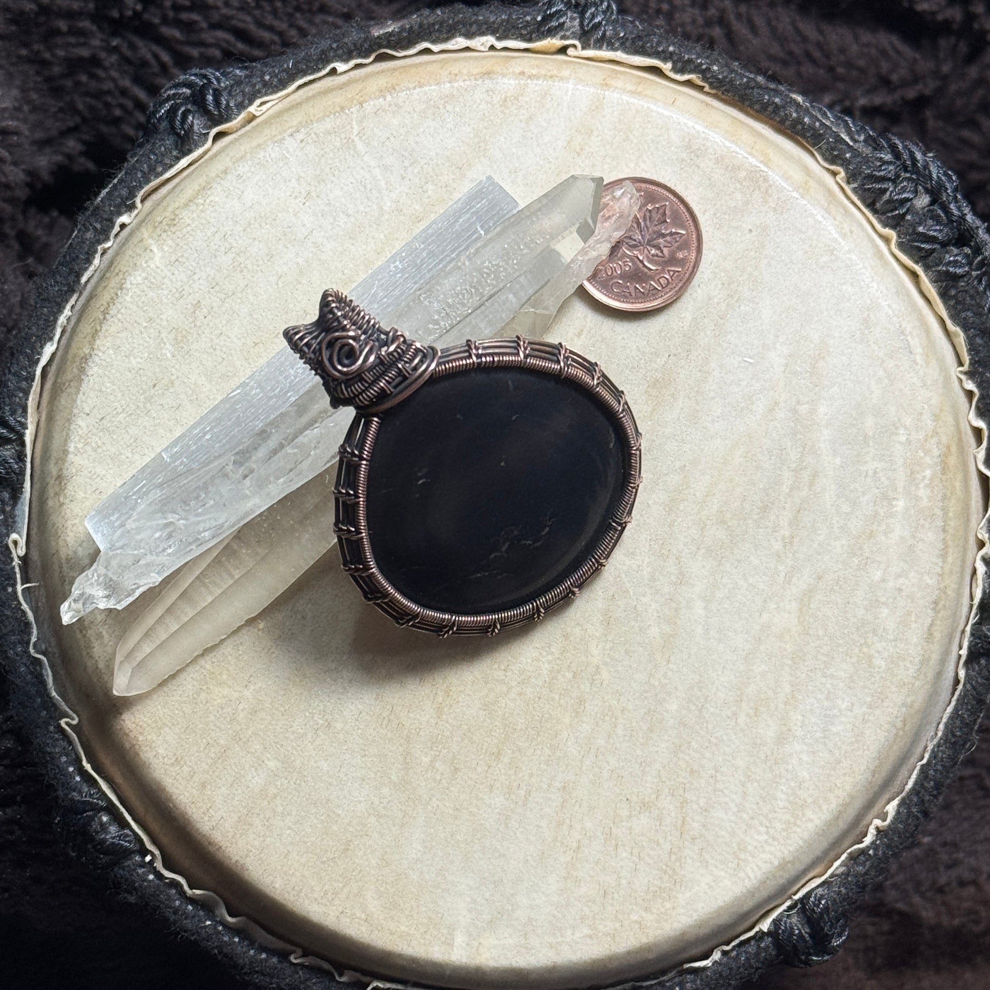 Front display view of a dark shungite pendant wrapped in patinated copper with intricate fine-wire weaving and subtle natural pyrite flecks.