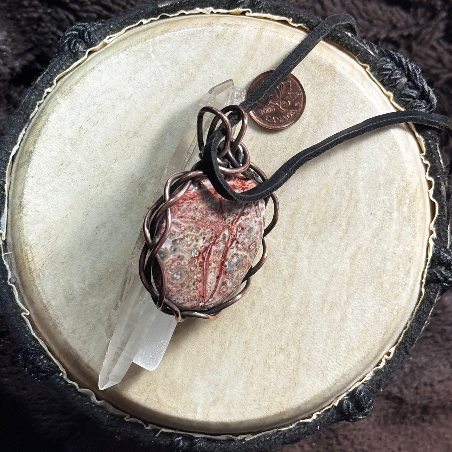 Side display view of a handmade Leopardskin Jasper pendant wrapped in reclaimed patinated copper and shown with reclaimed leather cord.
