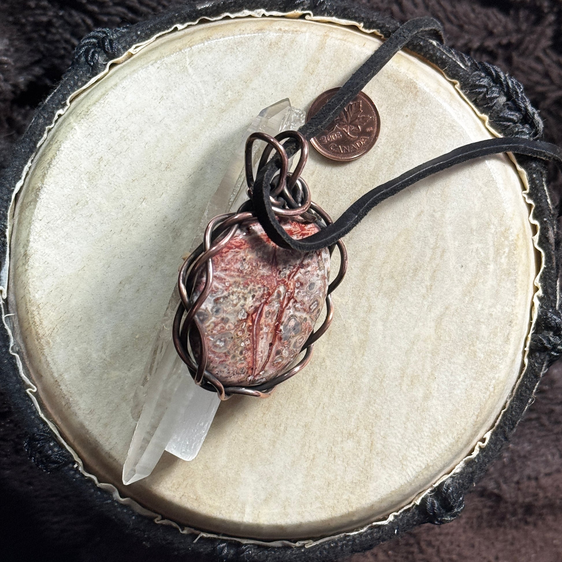 Side display view of a handmade Leopardskin Jasper pendant wrapped in reclaimed patinated copper and shown with reclaimed leather cord.
