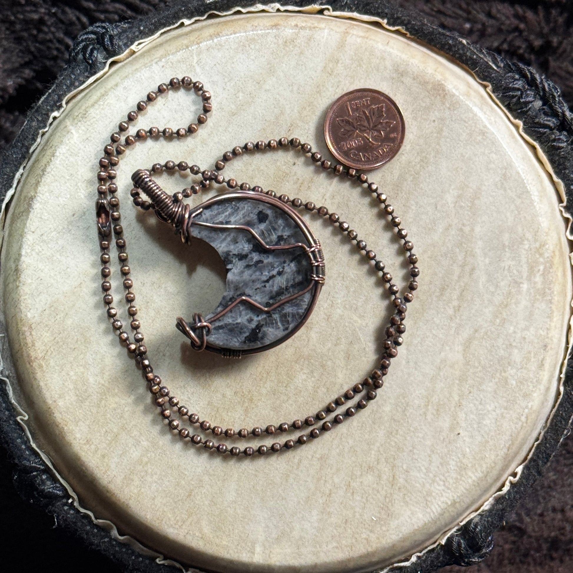 Reverse view of a handcrafted larvikite moon pendant in patinated copper showing the back wirework and faceted copper ball chain.
