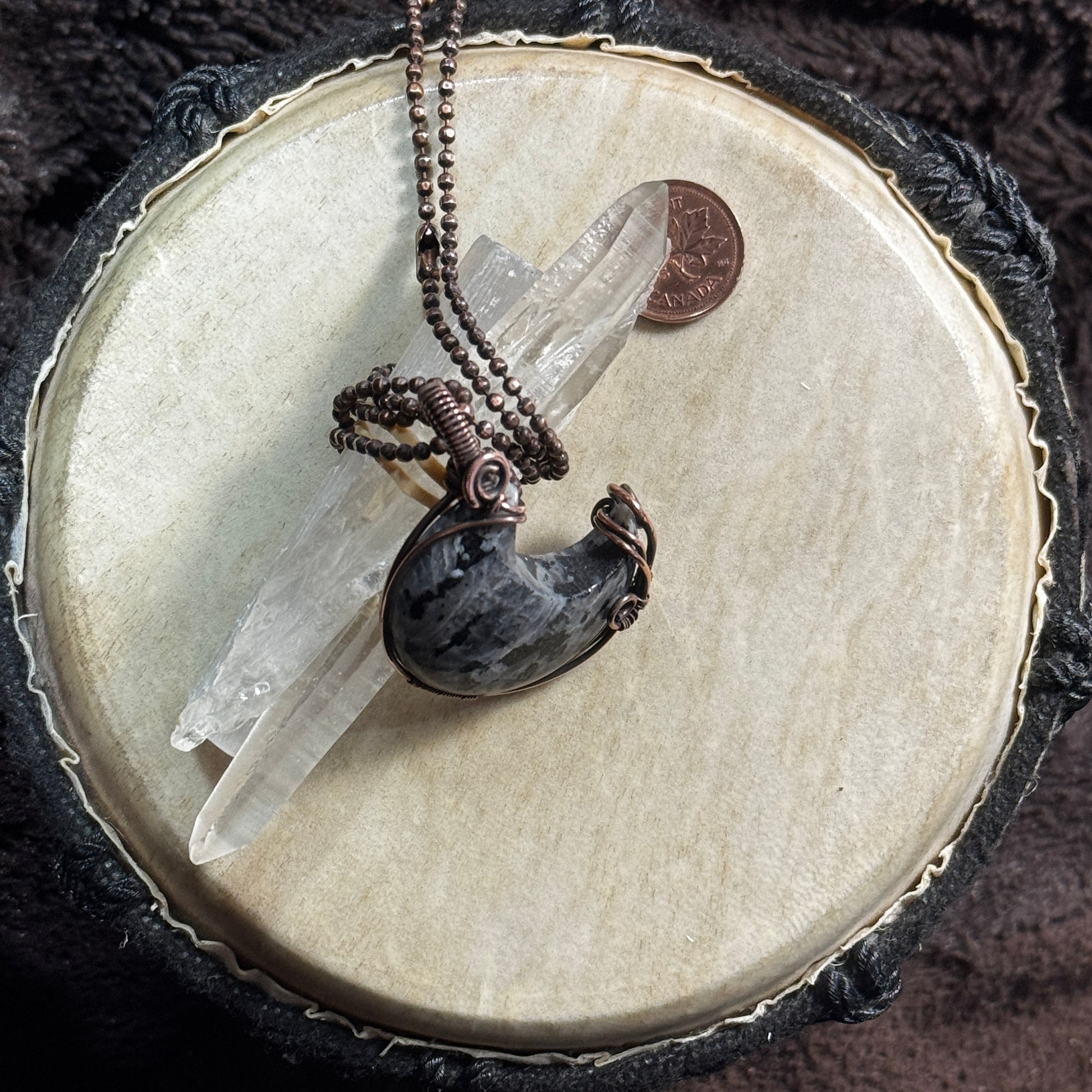Larvikite crescent moon necklace in patinated copper displayed with clear crystal points, showing the stone’s shape and subtle flash.