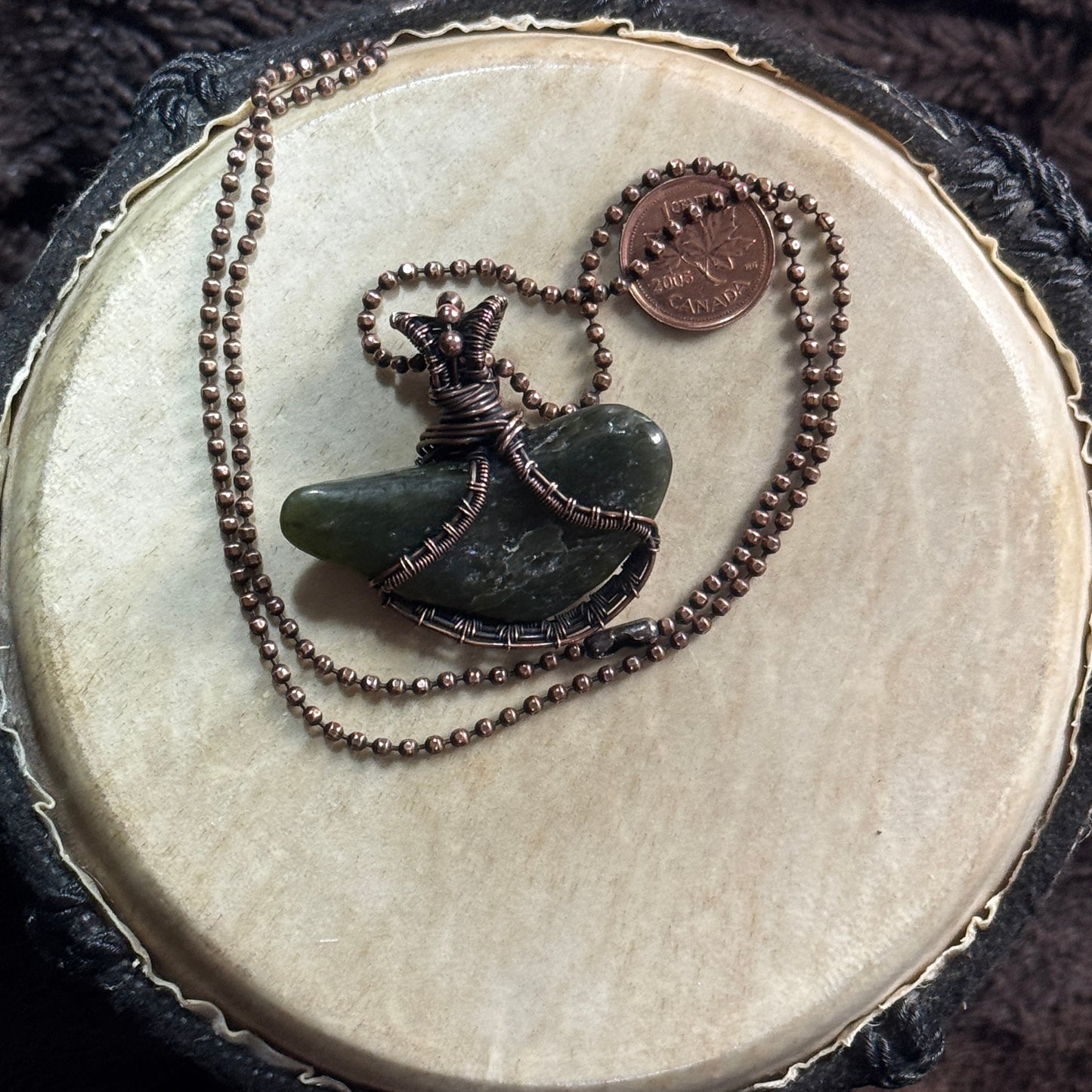 Reverse view of a tumbled British Columbia jade pendant showing its organic shape and hand-wrapped patinated copper setting.
