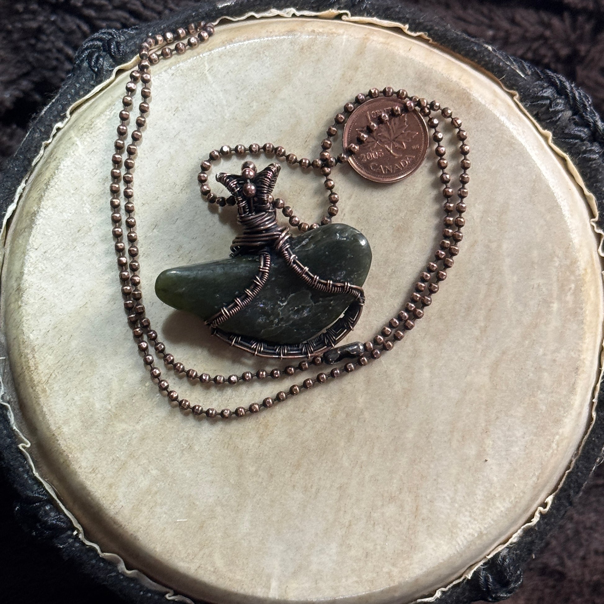 Reverse view of a tumbled British Columbia jade pendant showing its organic shape and hand-wrapped patinated copper setting.
