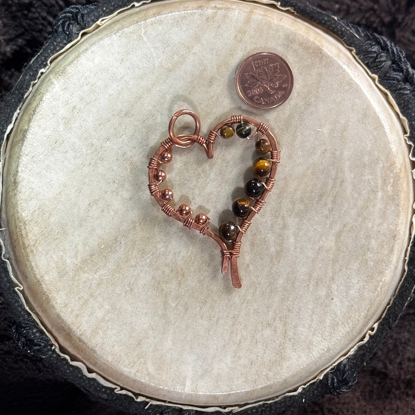 Front view of a handmade yellow tiger's eye heart pendant in hand-planished raw copper with raw copper bead embellishments.