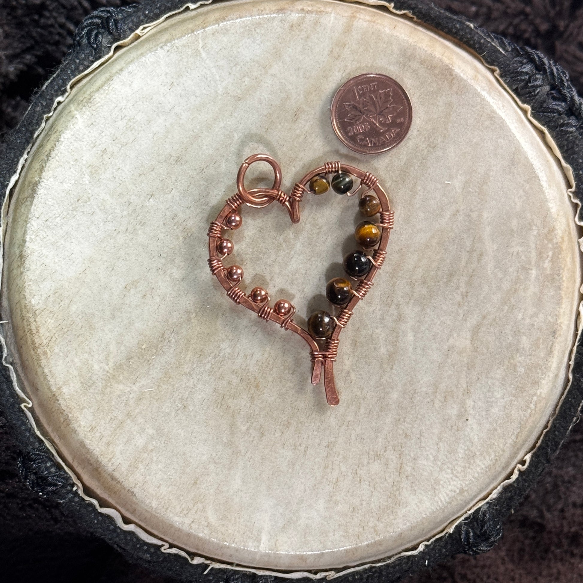 Front view of a handmade yellow tiger's eye heart pendant in hand-planished raw copper with raw copper bead embellishments.