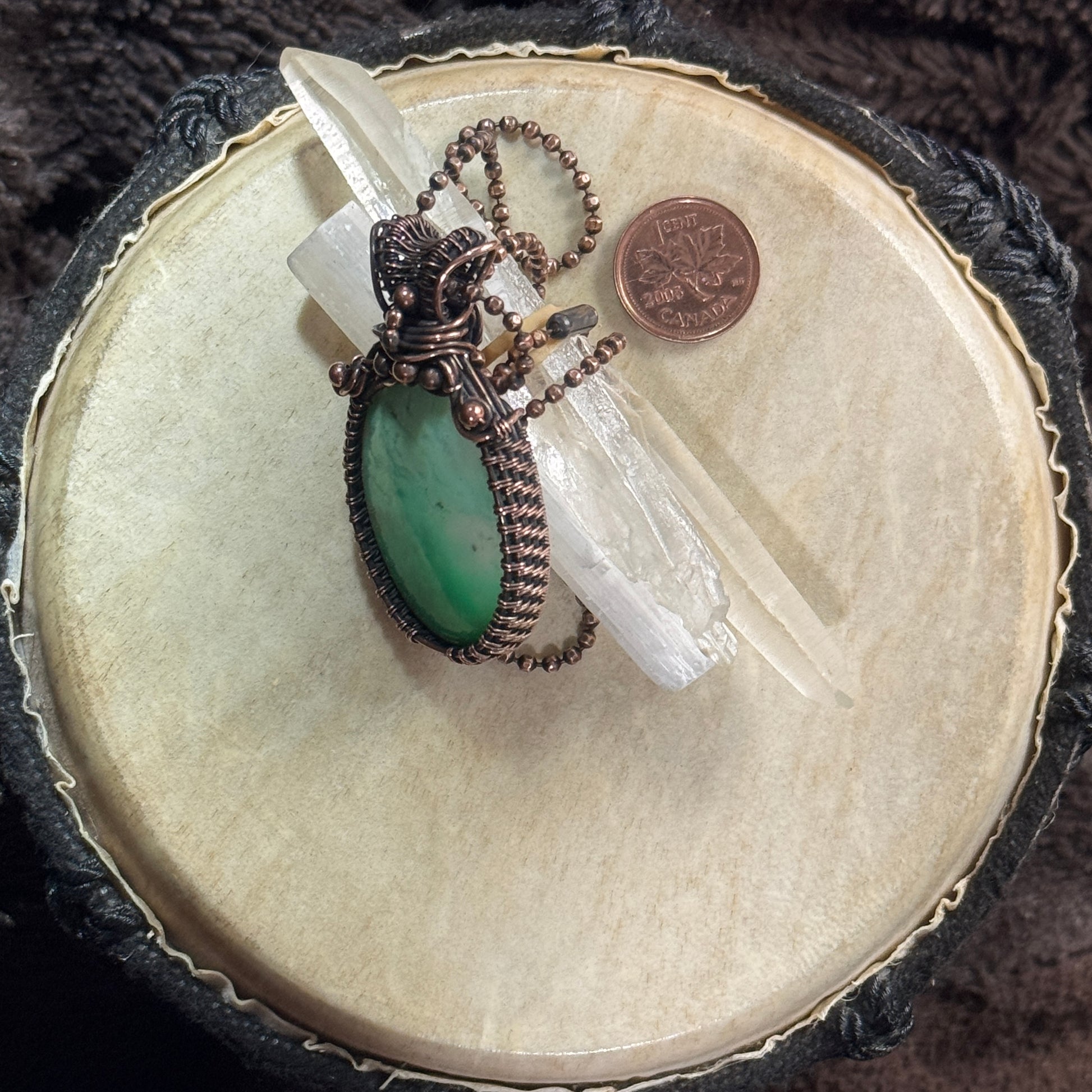 Side view of a patinated copper agatized chrysoprase pendant displayed with a clear crystal to show the profile and depth of the setting.
